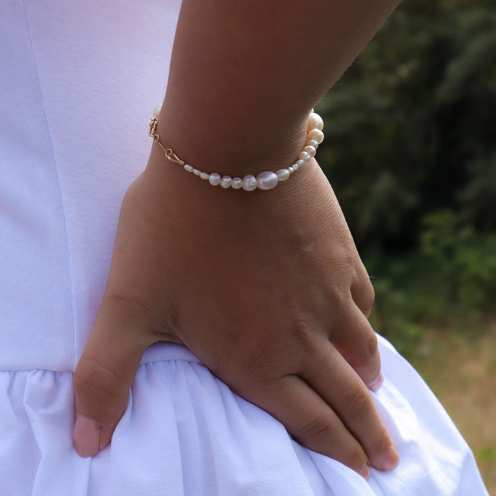 Hand wearing a pearl bracelet with a blurred natural background