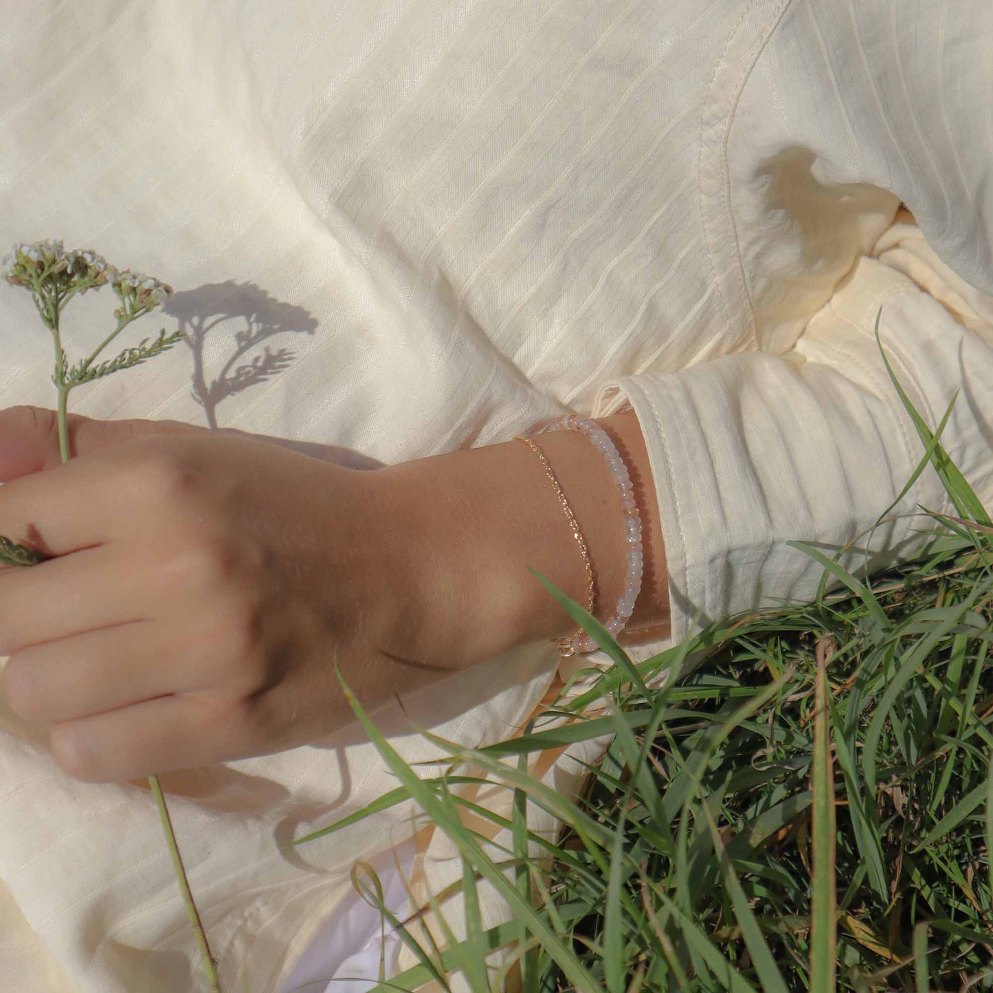 Person wearing a bracelet holding a flower, sitting on grass