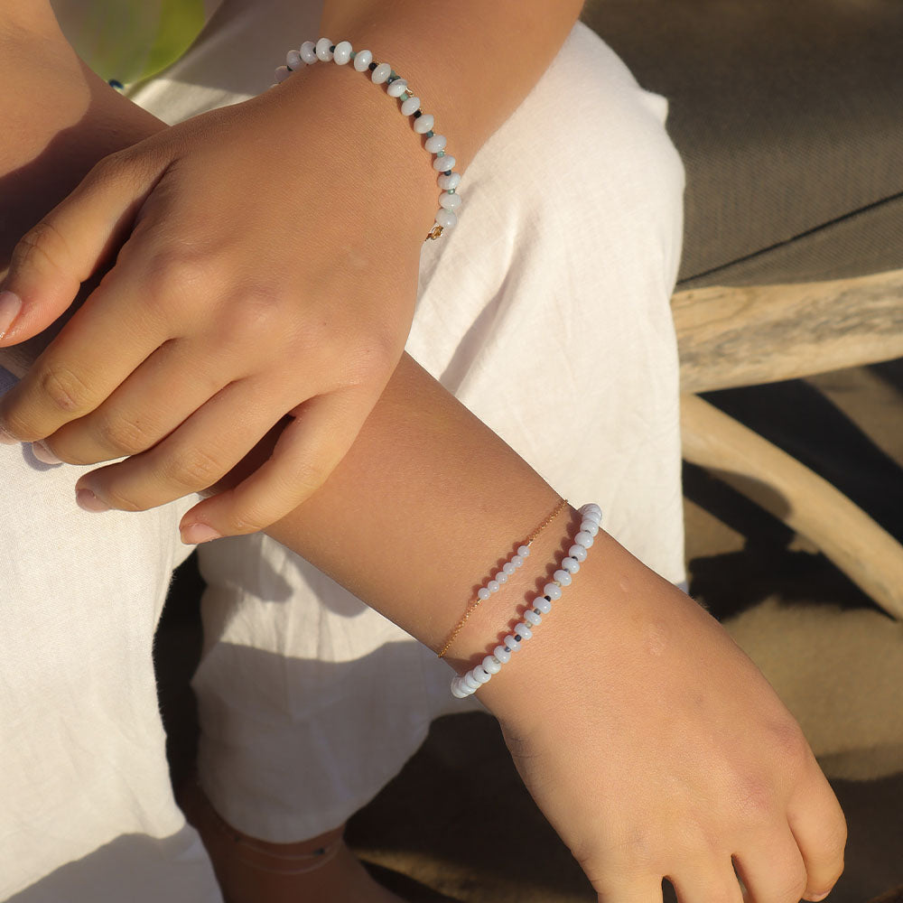 Close-up of a person's wrist wearing two beaded bracelets with a blurred background.