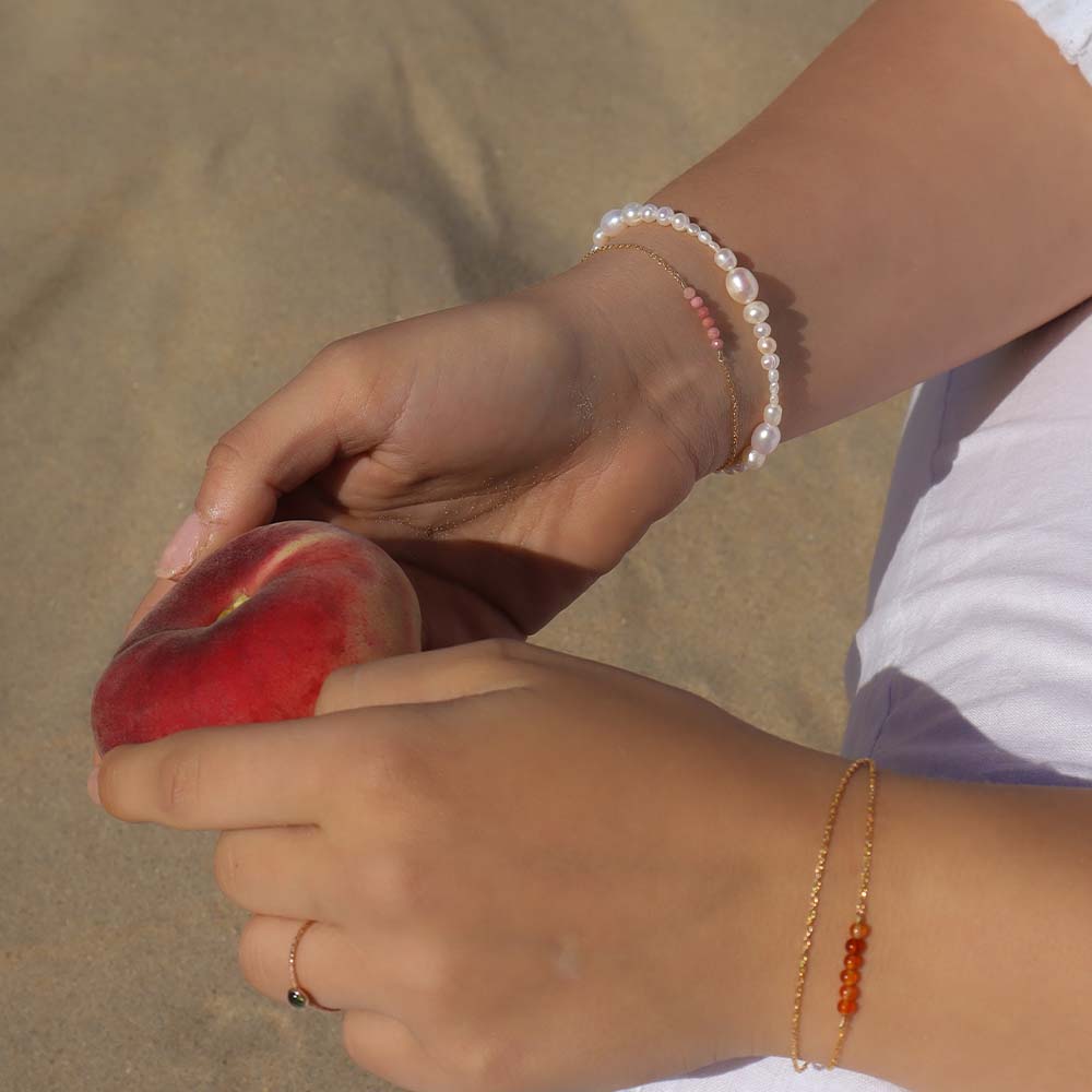 Person holding a red fruit with bracelets on a beige background