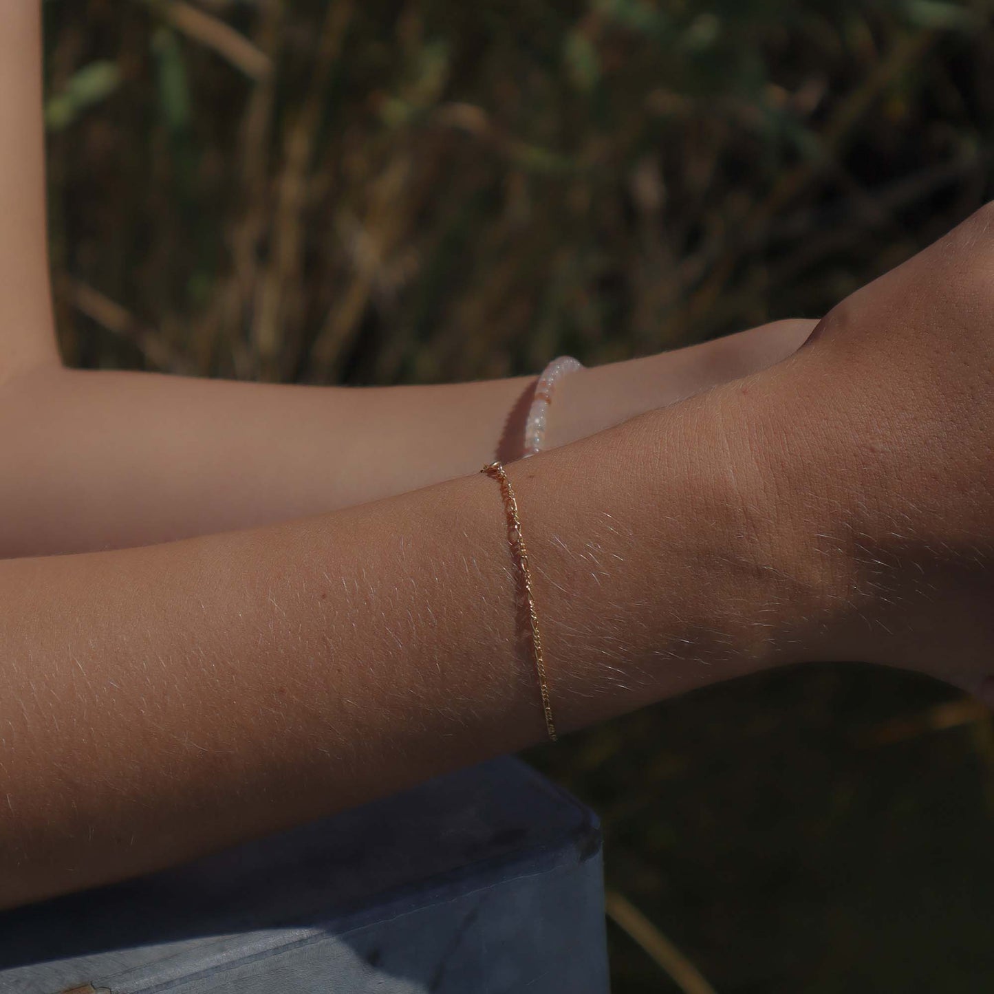 Close-up of a person's arm wearing a bracelet with a blurred natural background