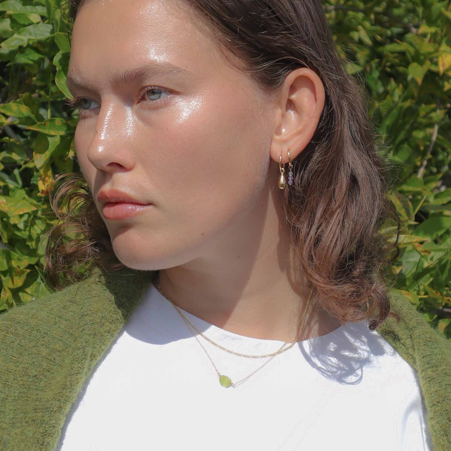 Woman wearing earrings with a green jacket and white shirt against a leafy background