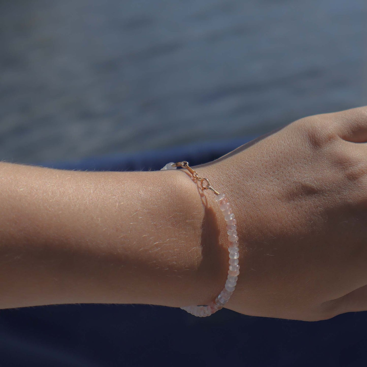 Close-up of a wrist wearing a pink bracelet with a blurred water background
