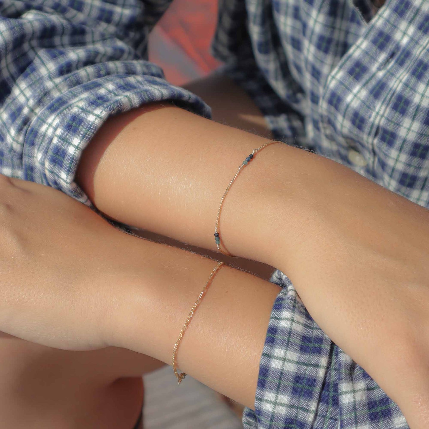 Close-up of a person wearing two thin gold bracelets on their wrist with a blurred background.