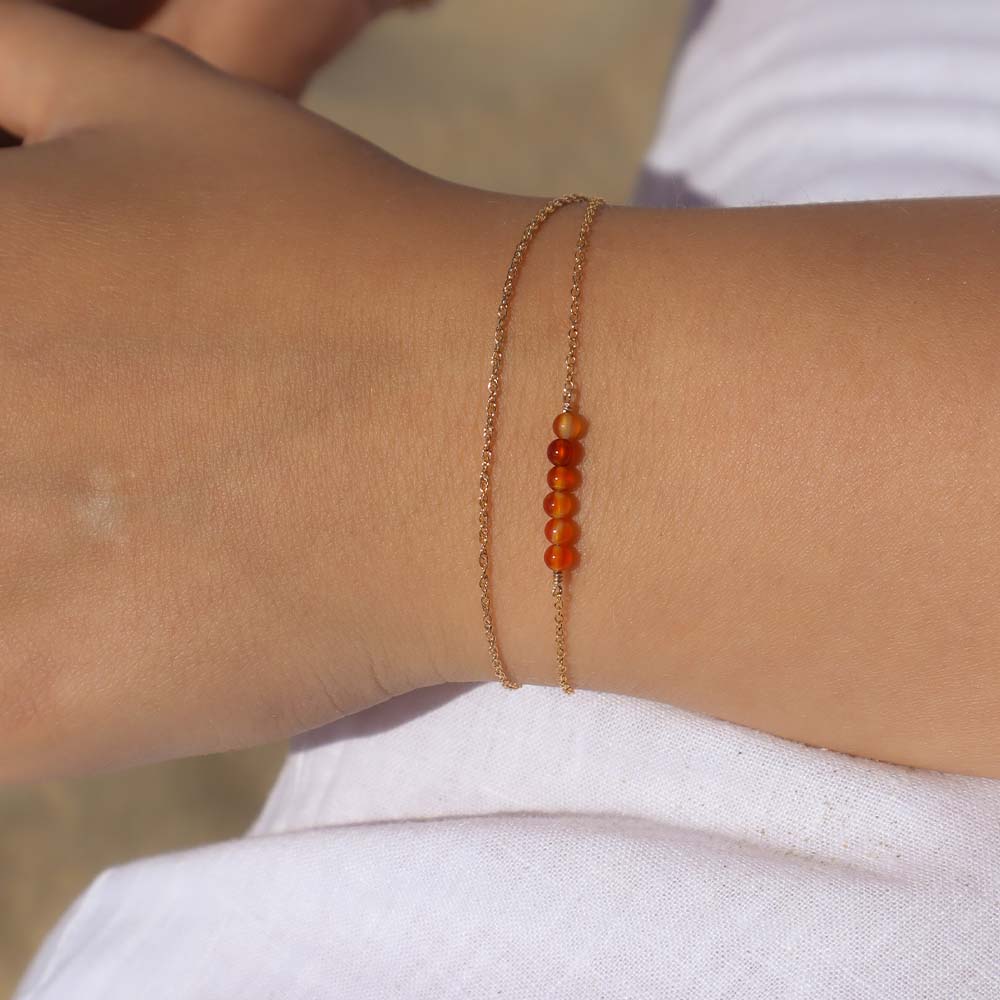 Close-up of a wrist wearing a gold bracelet with red beads against a blurred background