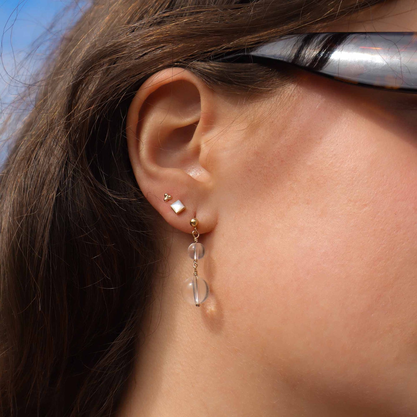 Close-up of an ear wearing a gold earring with a clear gemstone.