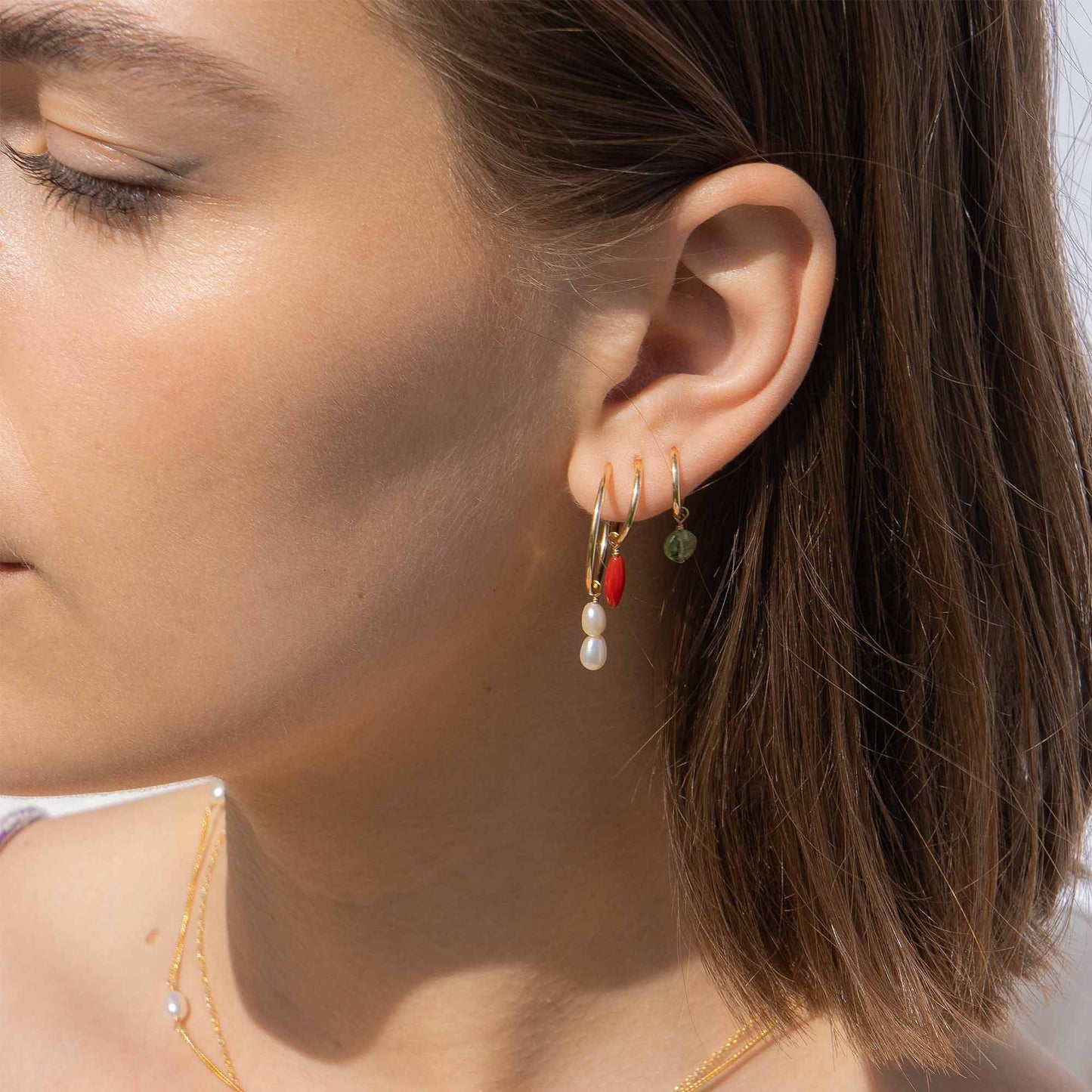 Close-up of a person wearing gold hoop earrings with colorful charms.