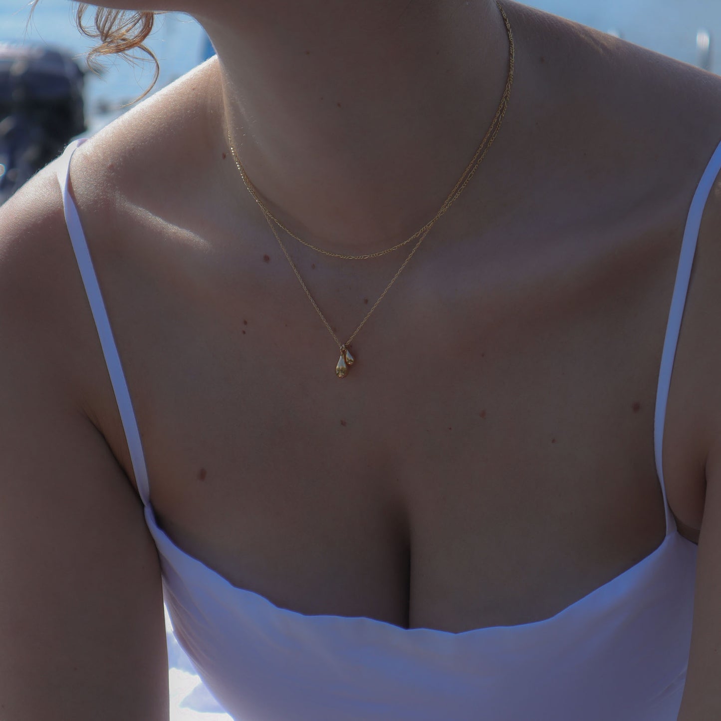 Close-up of a person wearing a gold necklace with a small pendant, outdoors.