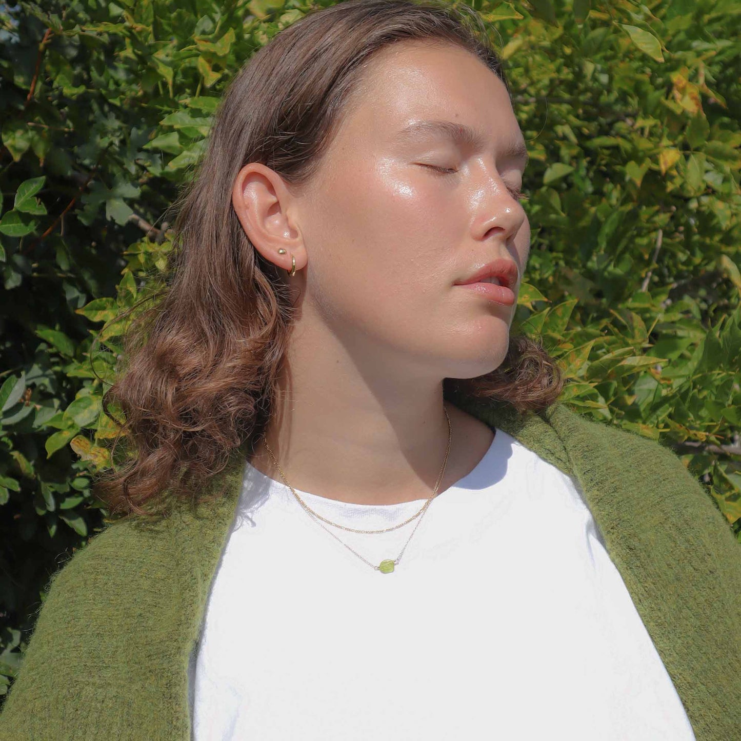 Person wearing a green cardigan and white shirt against a green leafy background