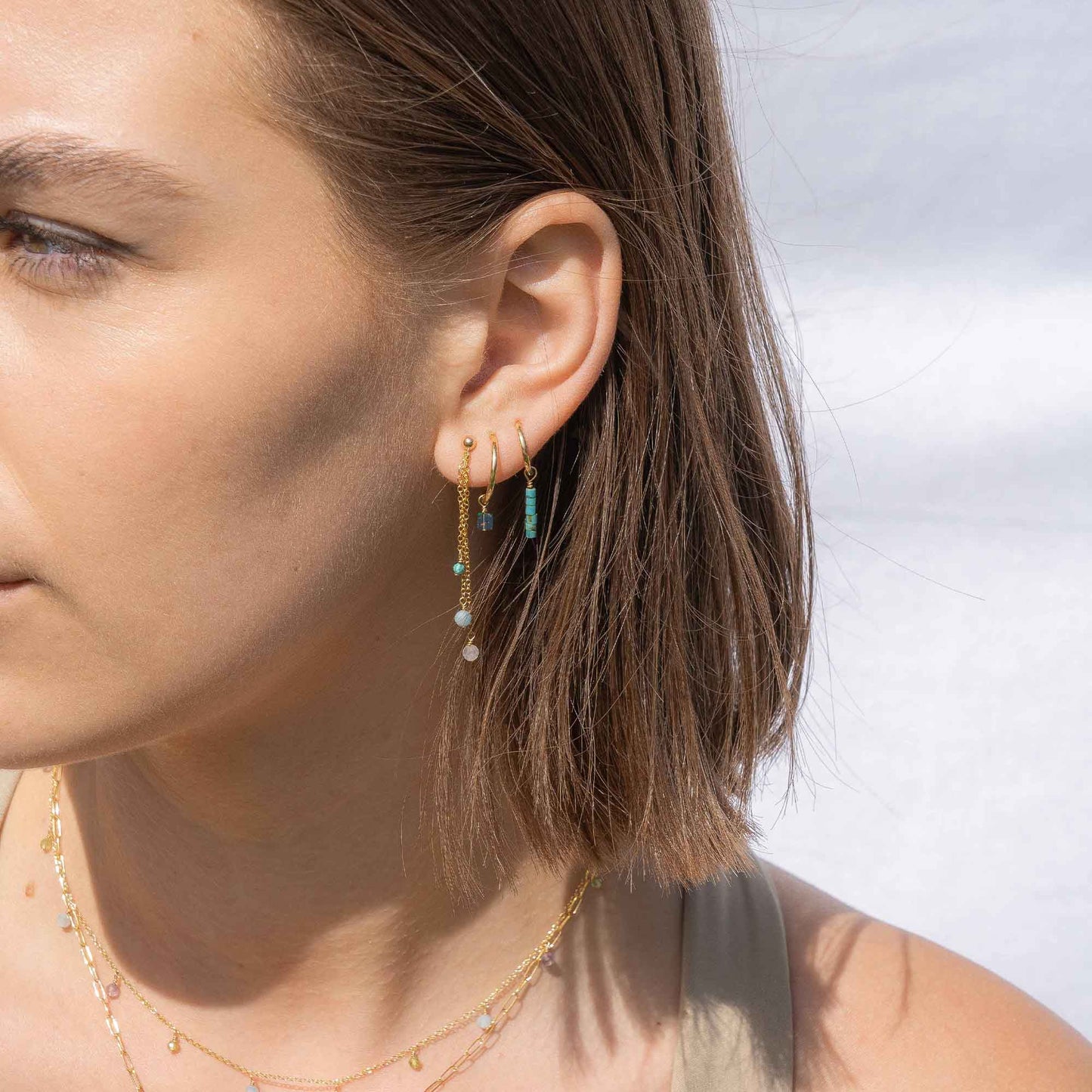 Close-up of a woman wearing gold earrings with green and clear beads against a blurred background
