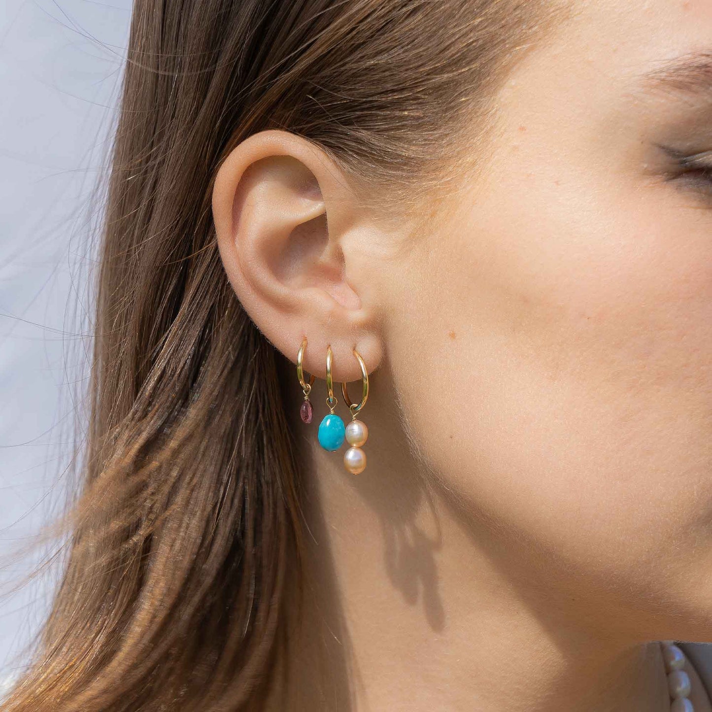 Close-up of a person wearing gold hoop earrings with colorful beads.