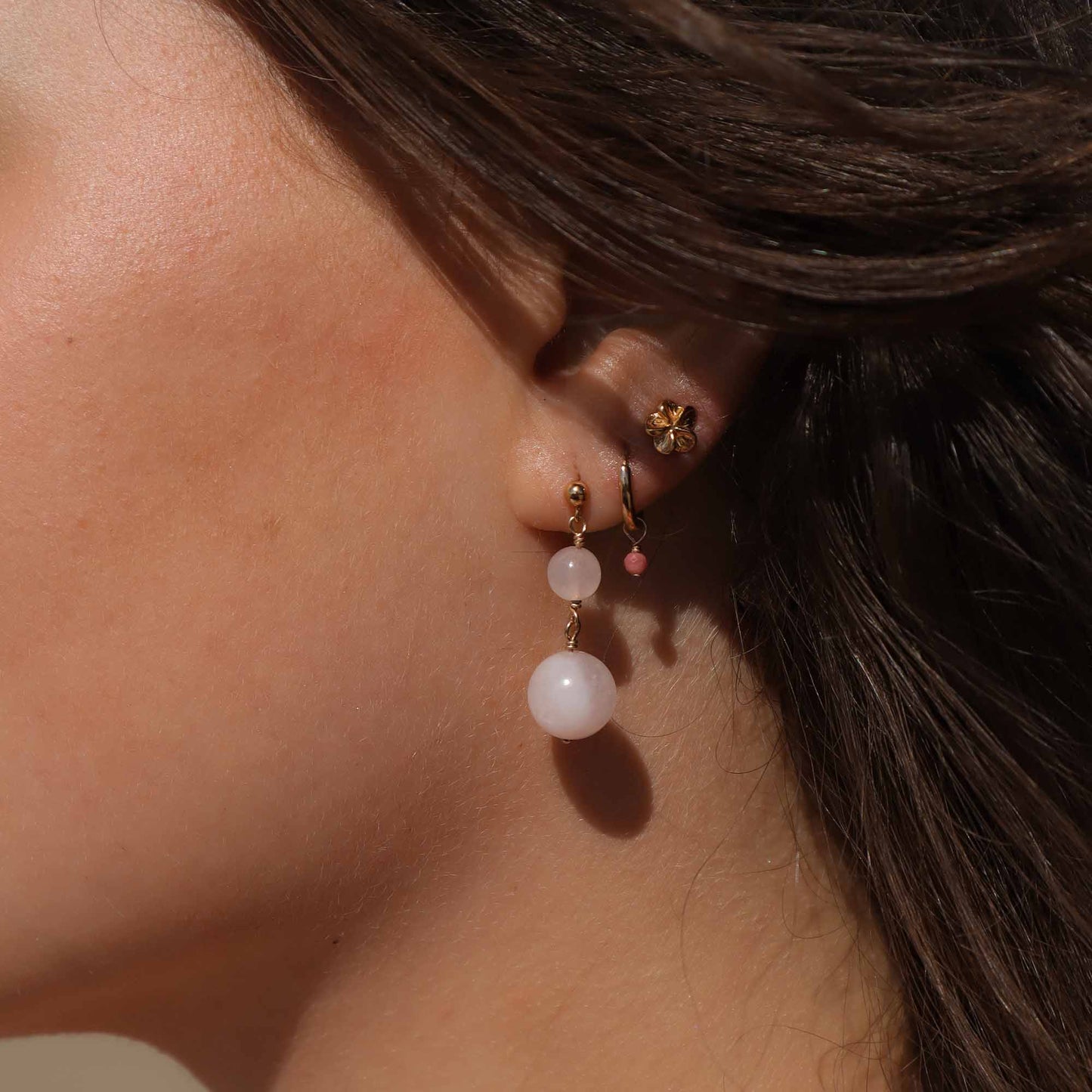 Close-up of an ear wearing a gold earring with pink beads.