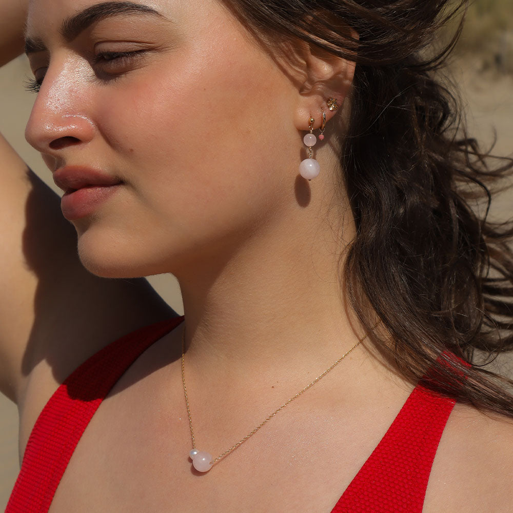 Woman wearing a red top and pearl necklace and earrings outdoors