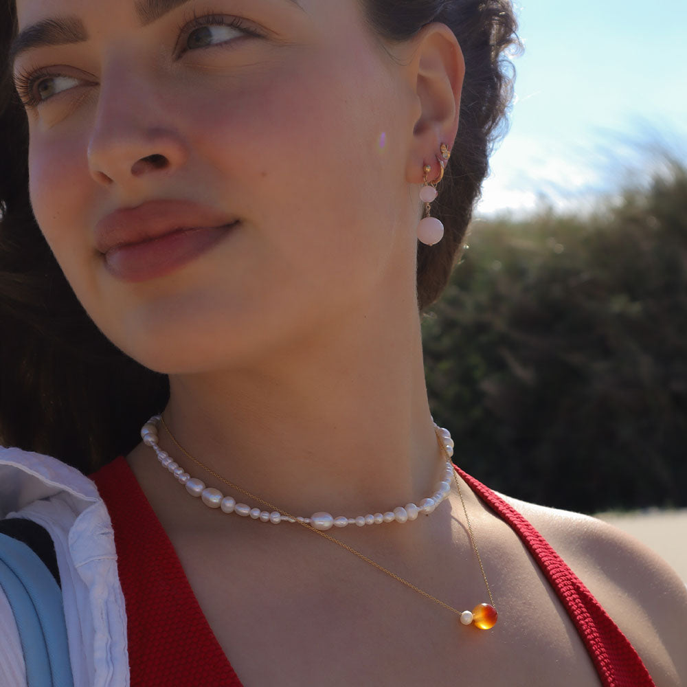 Close-up of a woman wearing a pearl necklace and earrings with a blurred natural background