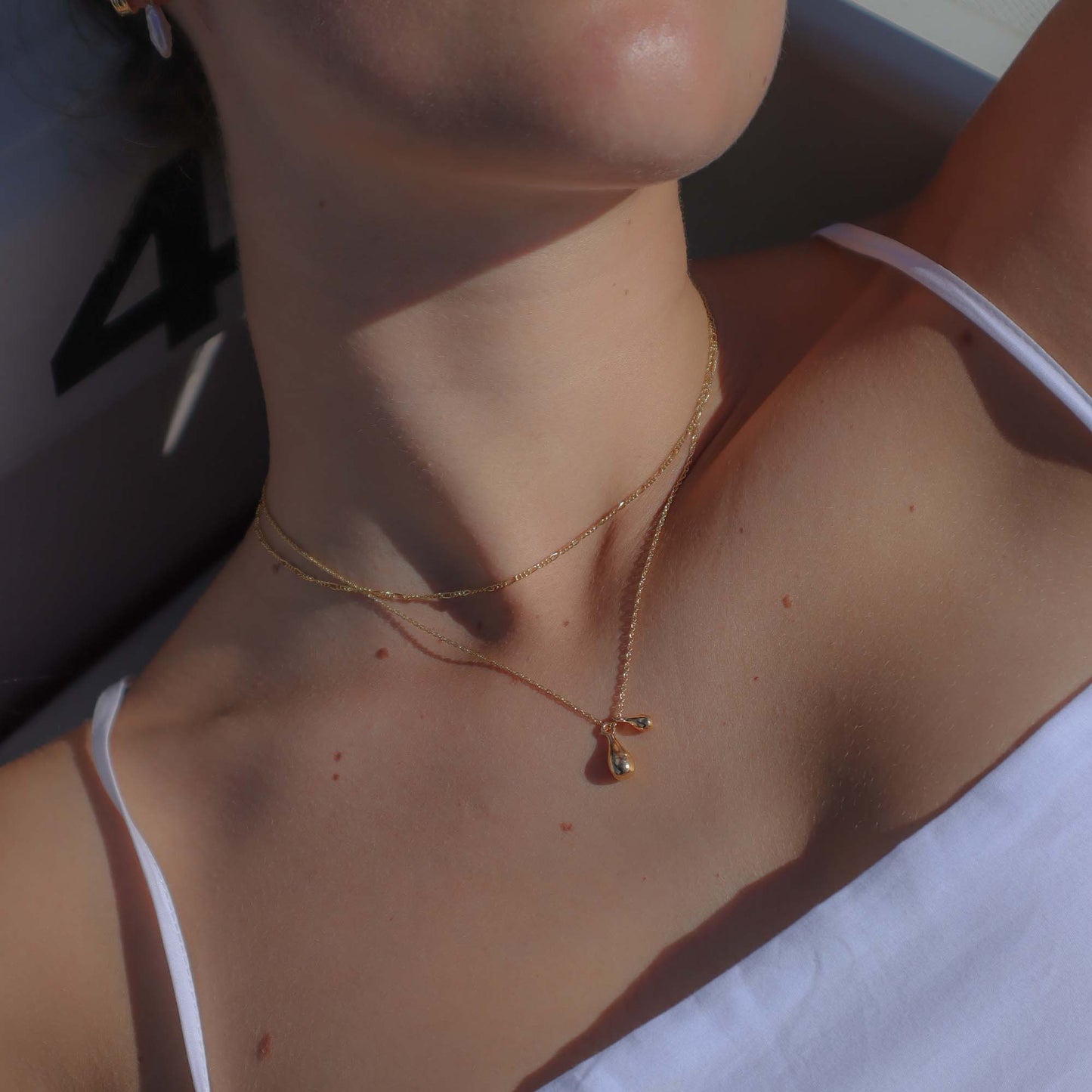 Close-up of a person wearing a gold necklace with a pendant.