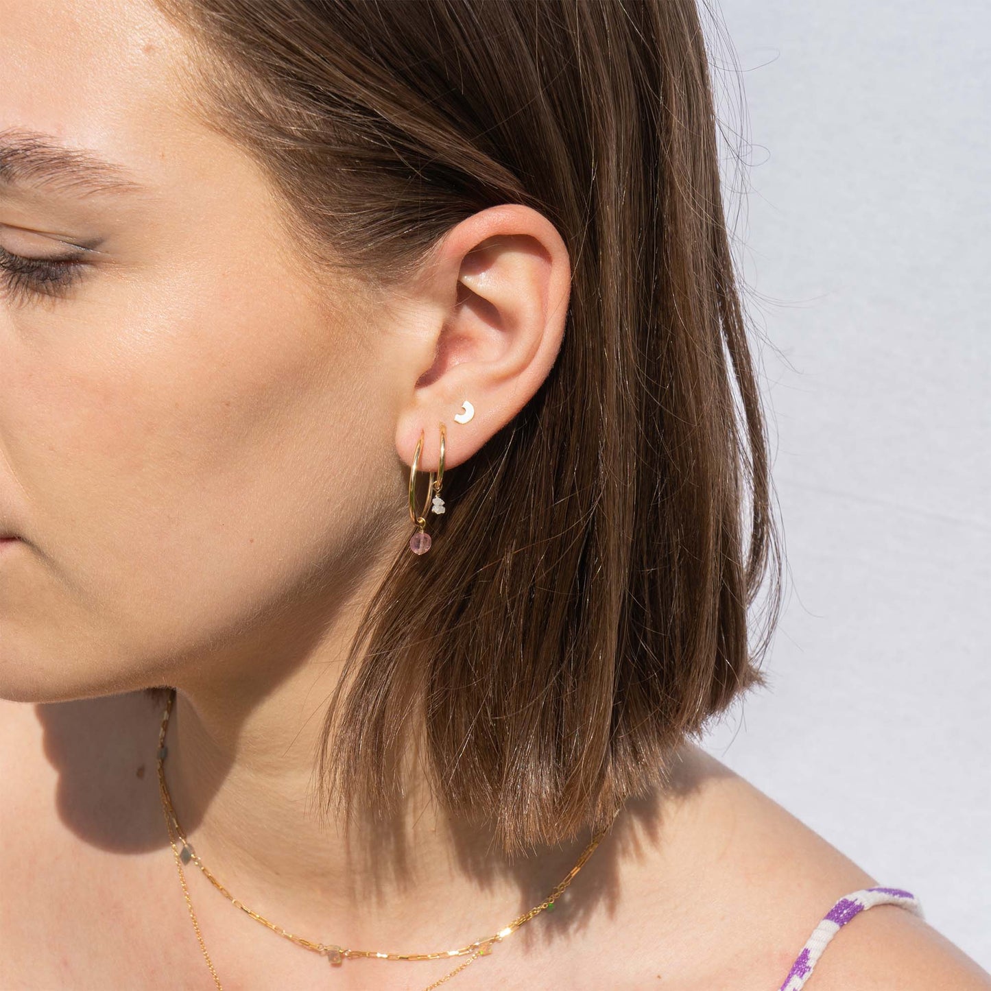 Close-up of a woman's ear wearing gold earrings with a plain background