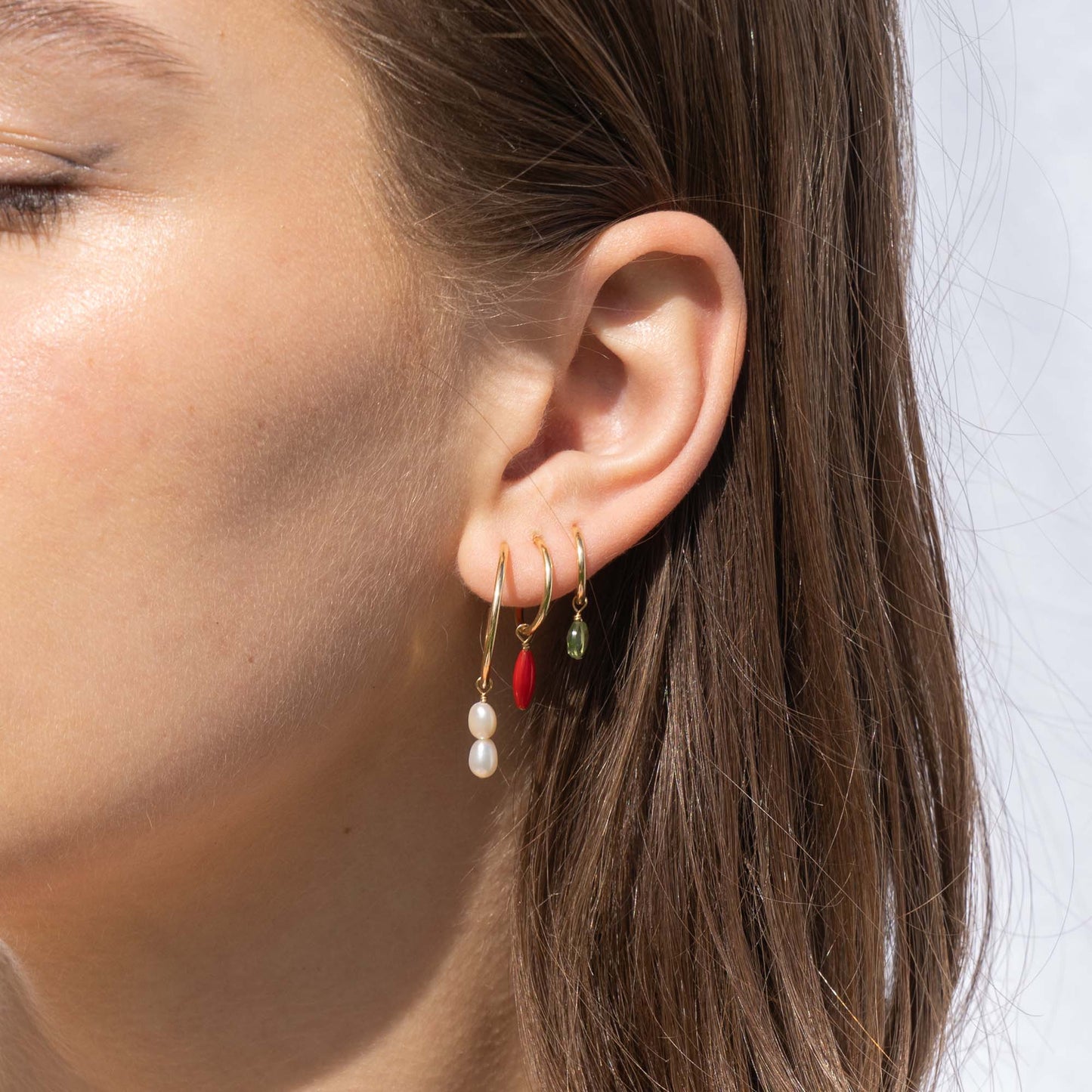 Close-up of an ear wearing three earrings with different colored beads.