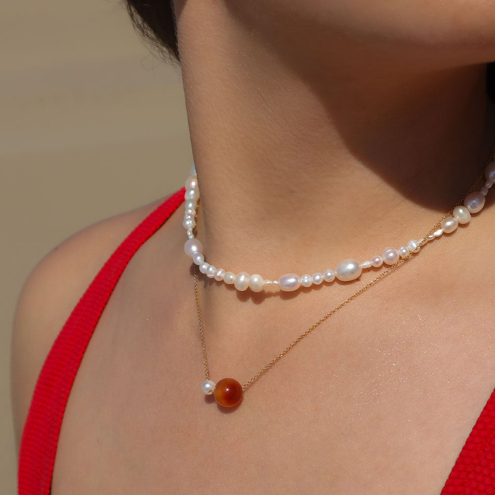 Pearl necklace with a red pendant worn by a person in a red top against a neutral background