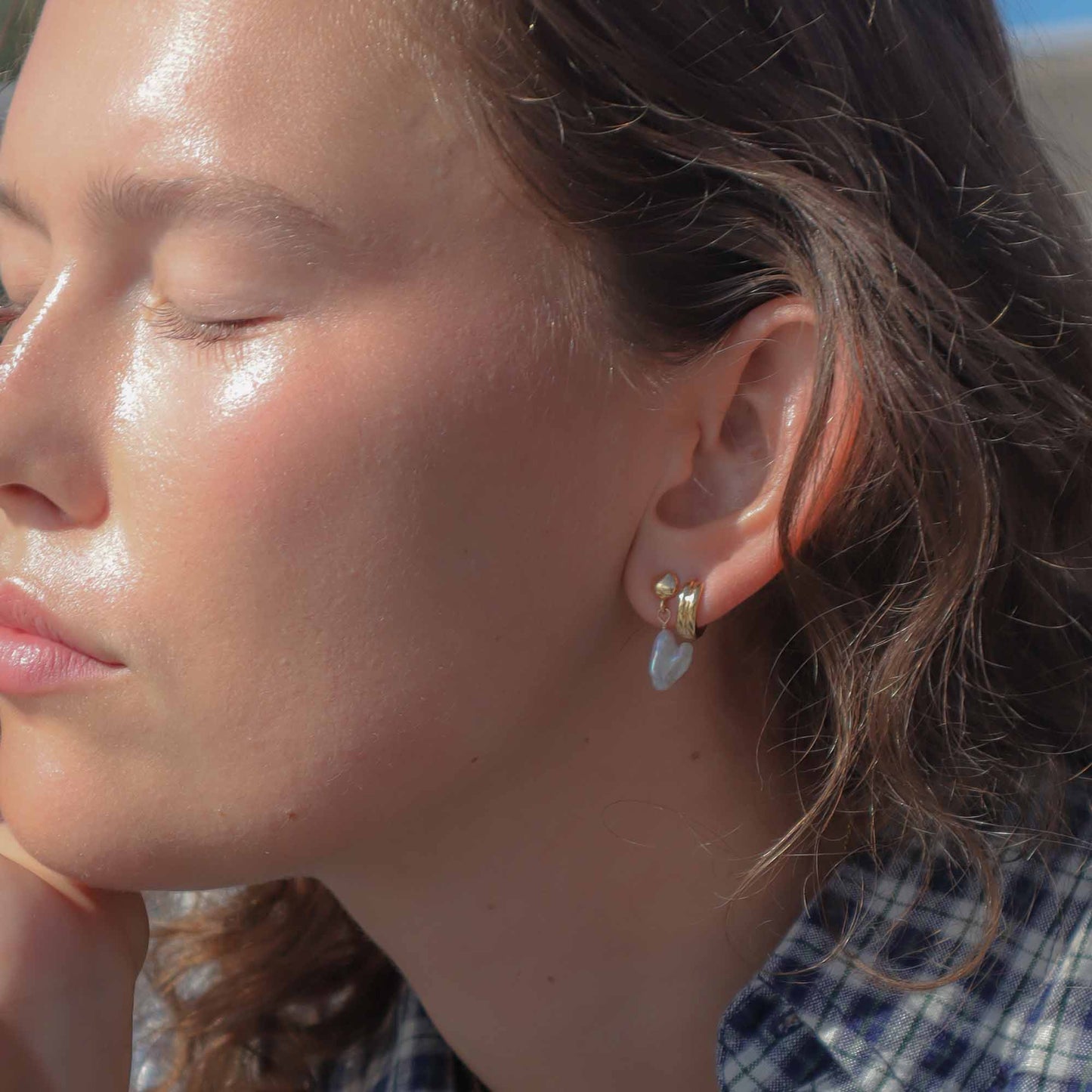 Close-up of a woman's face with sun-kissed skin, wearing gold and blue earrings.