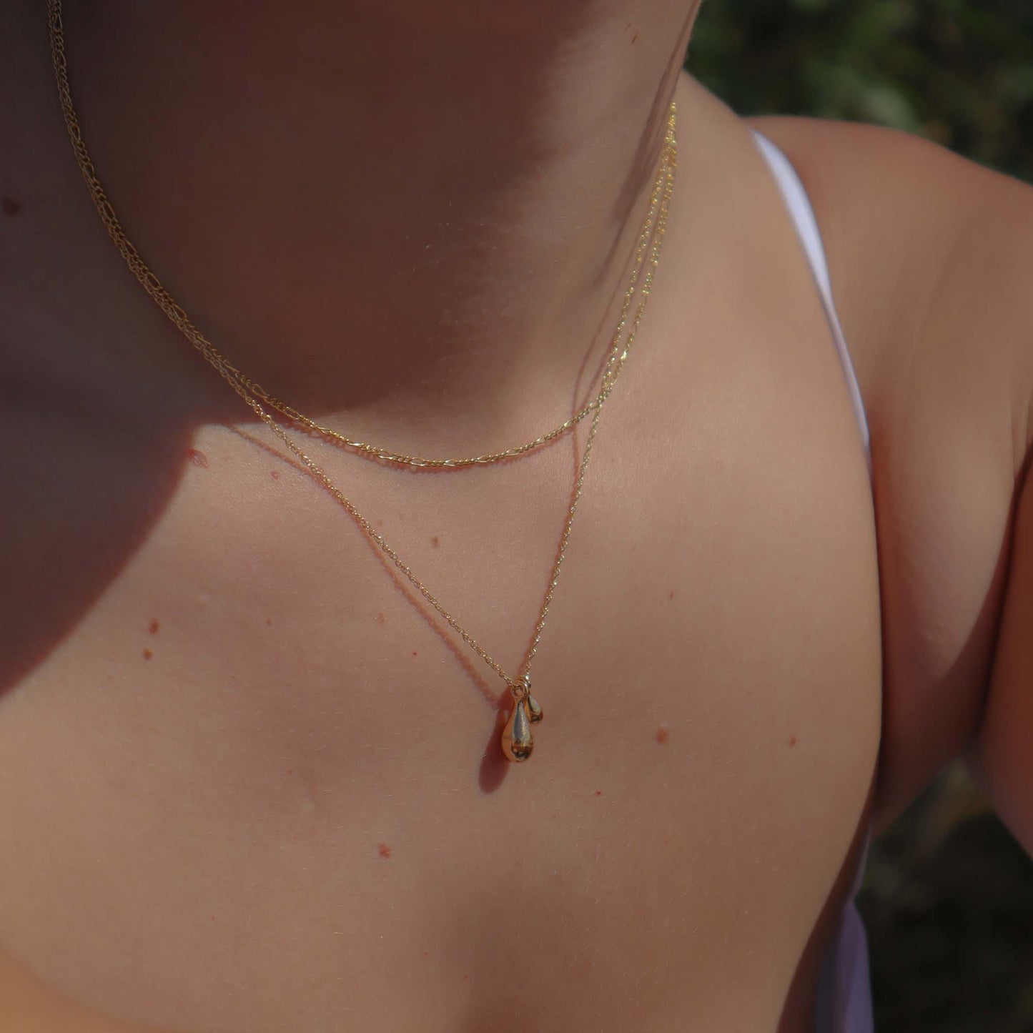 Close-up of a gold necklace with a pendant on a person's neck.