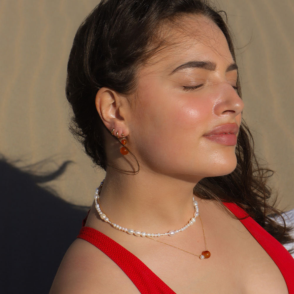 Woman wearing a red top and pearl necklace with orange beads against a neutral background