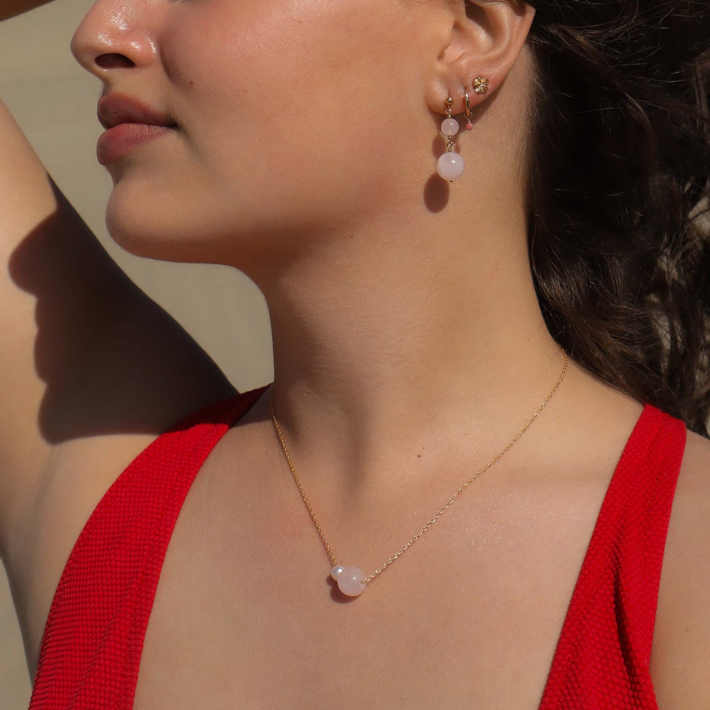 Close-up of a woman wearing a gold necklace and earrings with a neutral background