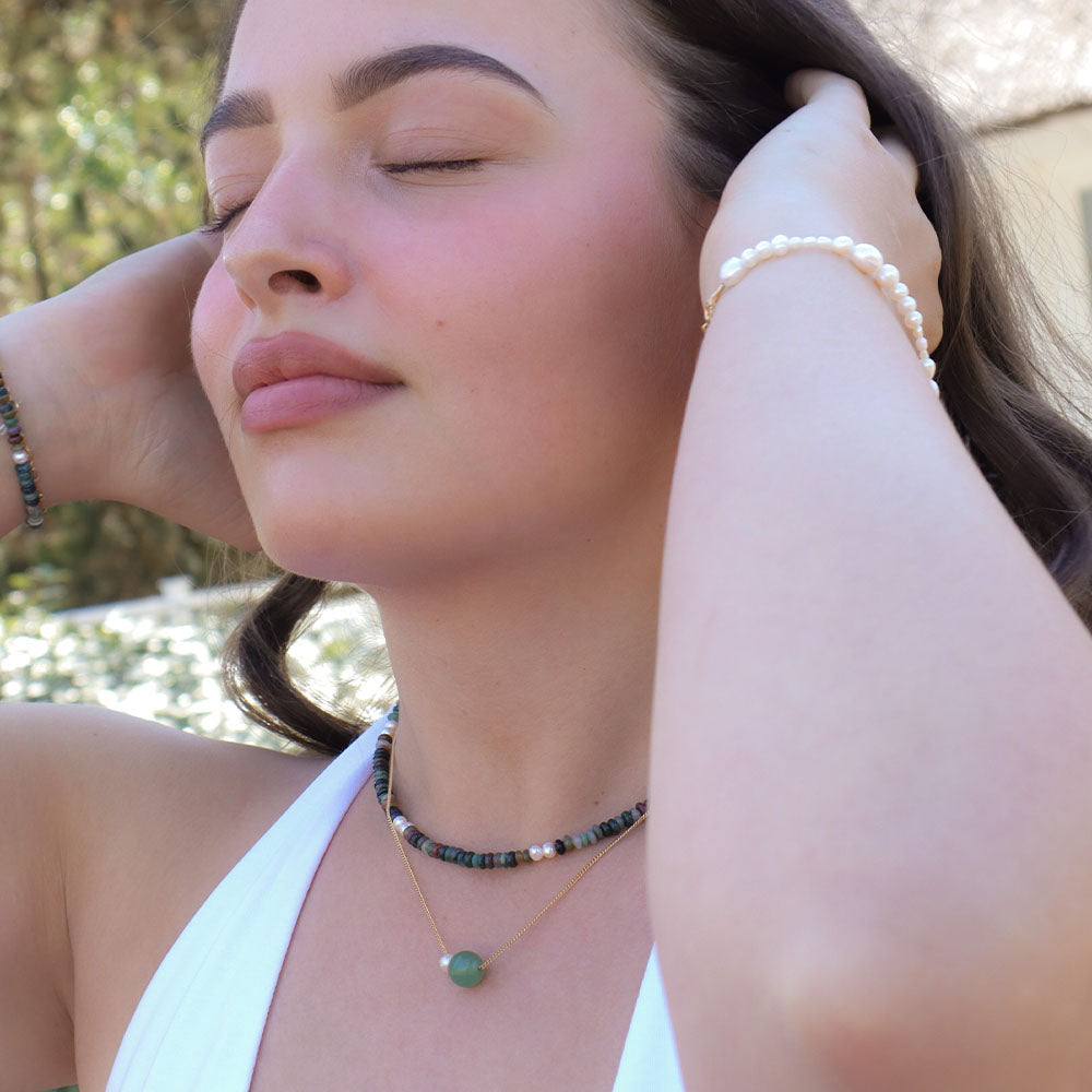 Woman wearing a necklace and bracelet with a blurred outdoor background