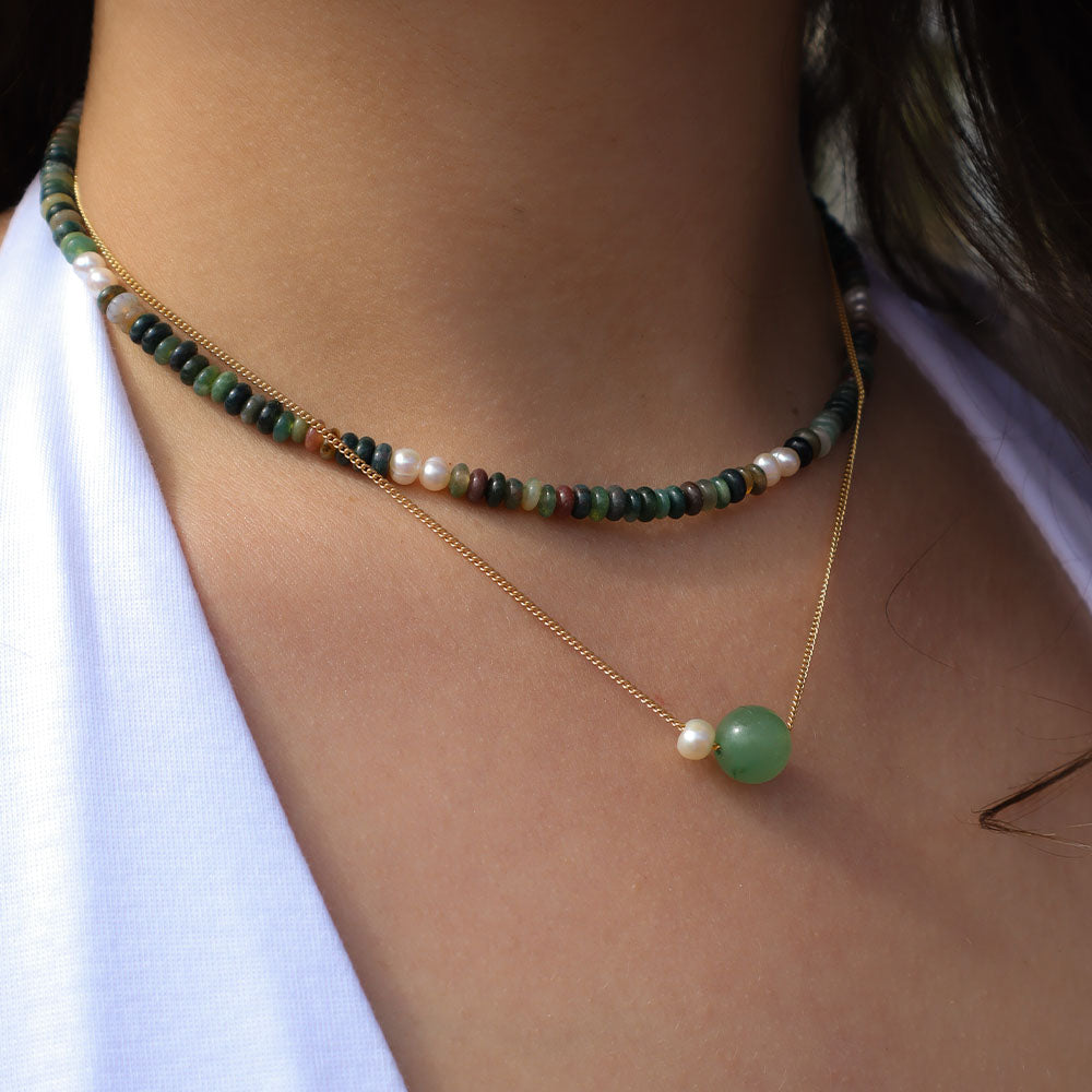 Necklace with green and gold beads on a person wearing a white shirt