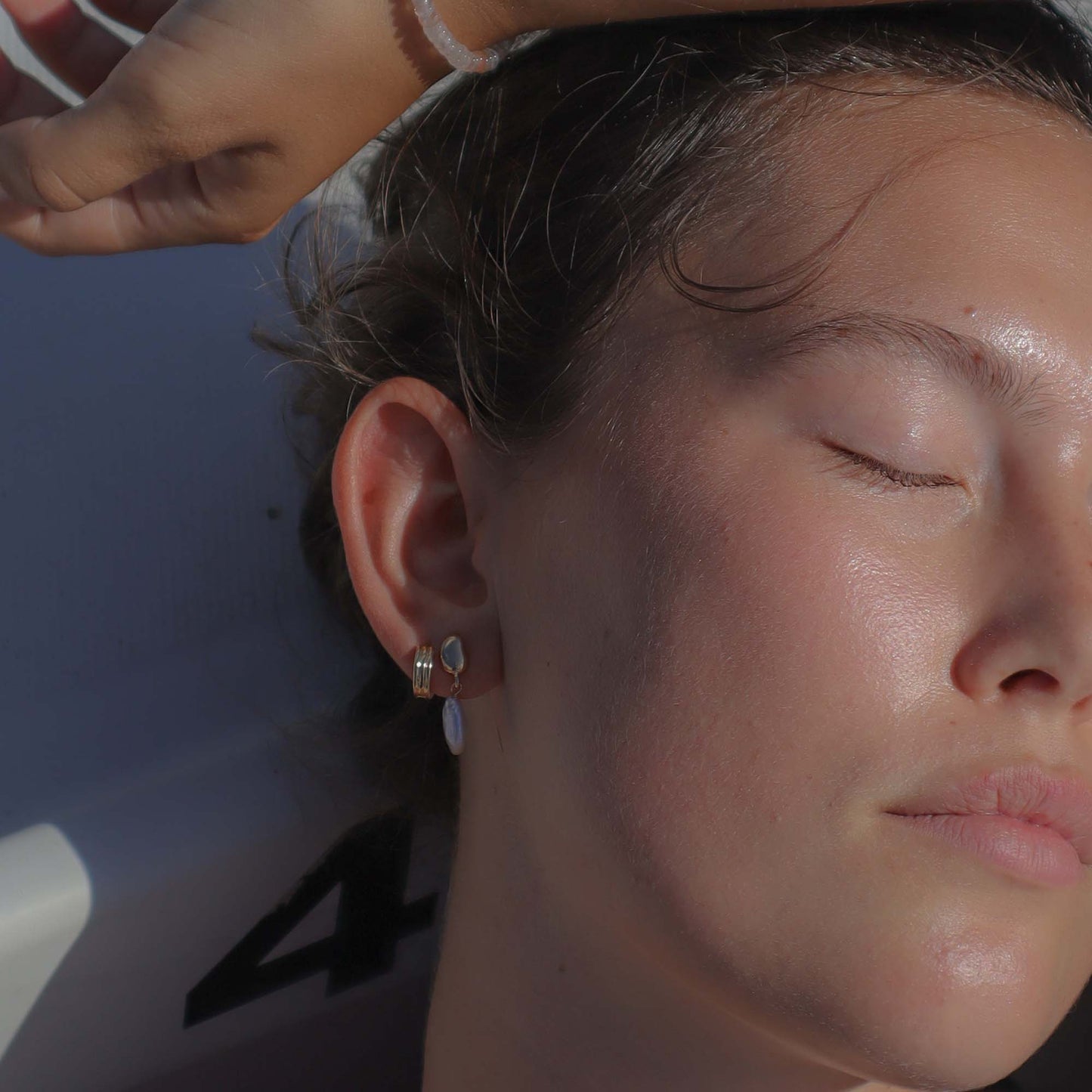 Close-up of a person with earrings, sun shining on their face