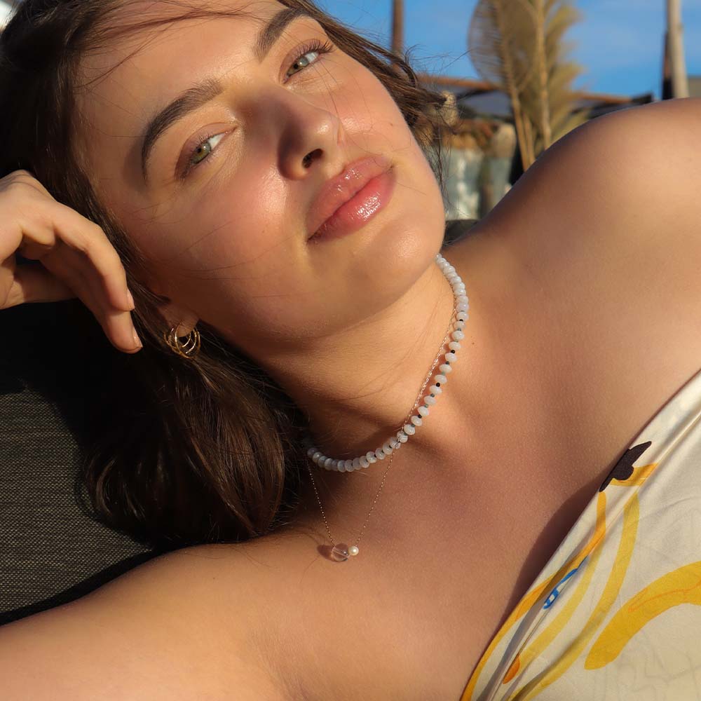 Woman with a relaxed expression outdoors, wearing a necklace.