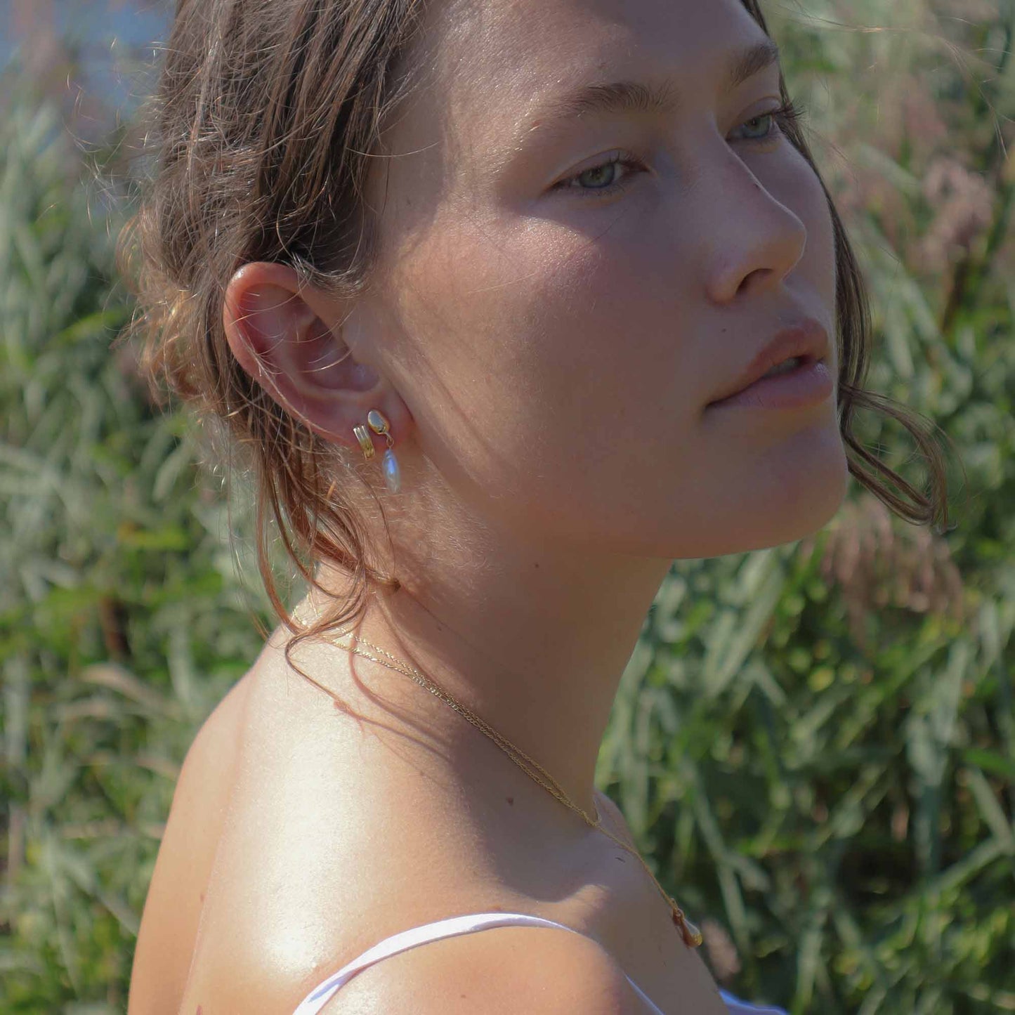 Woman with earrings and a necklace against a natural background