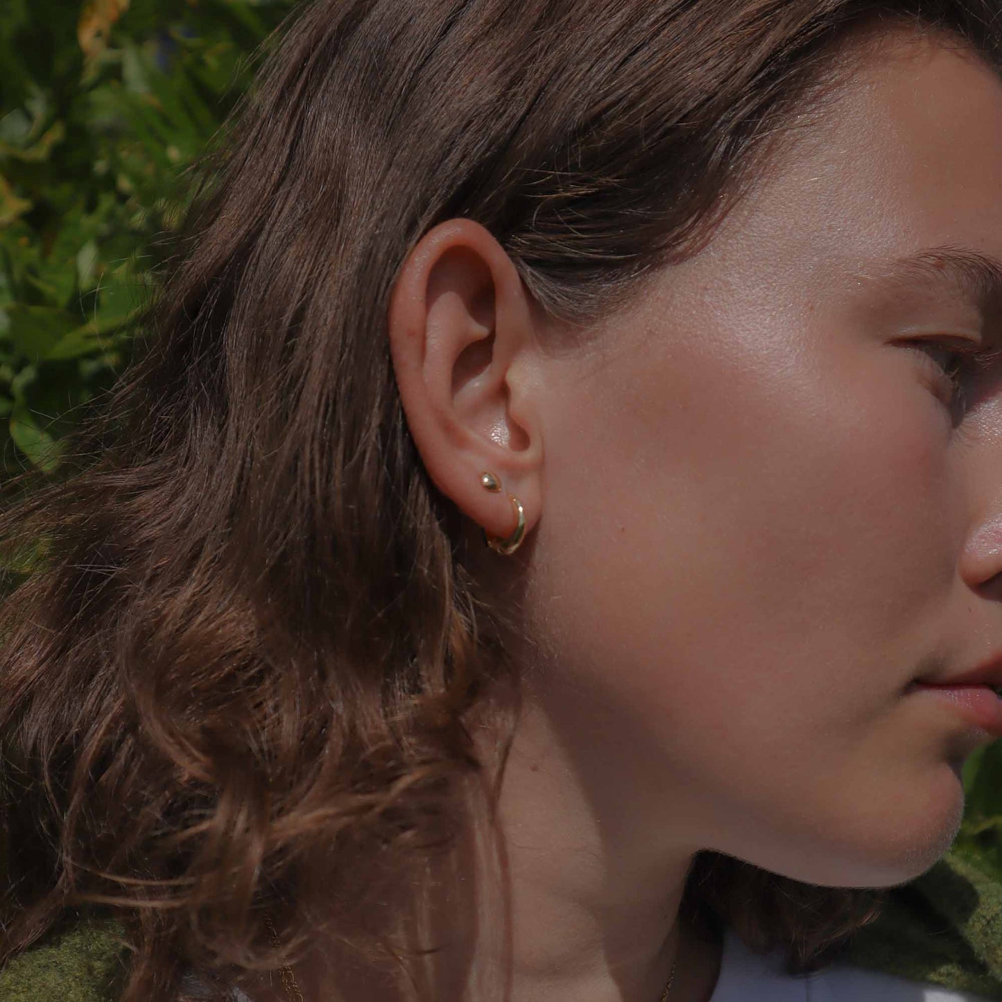 Close-up of a person wearing gold earrings with a blurred natural background