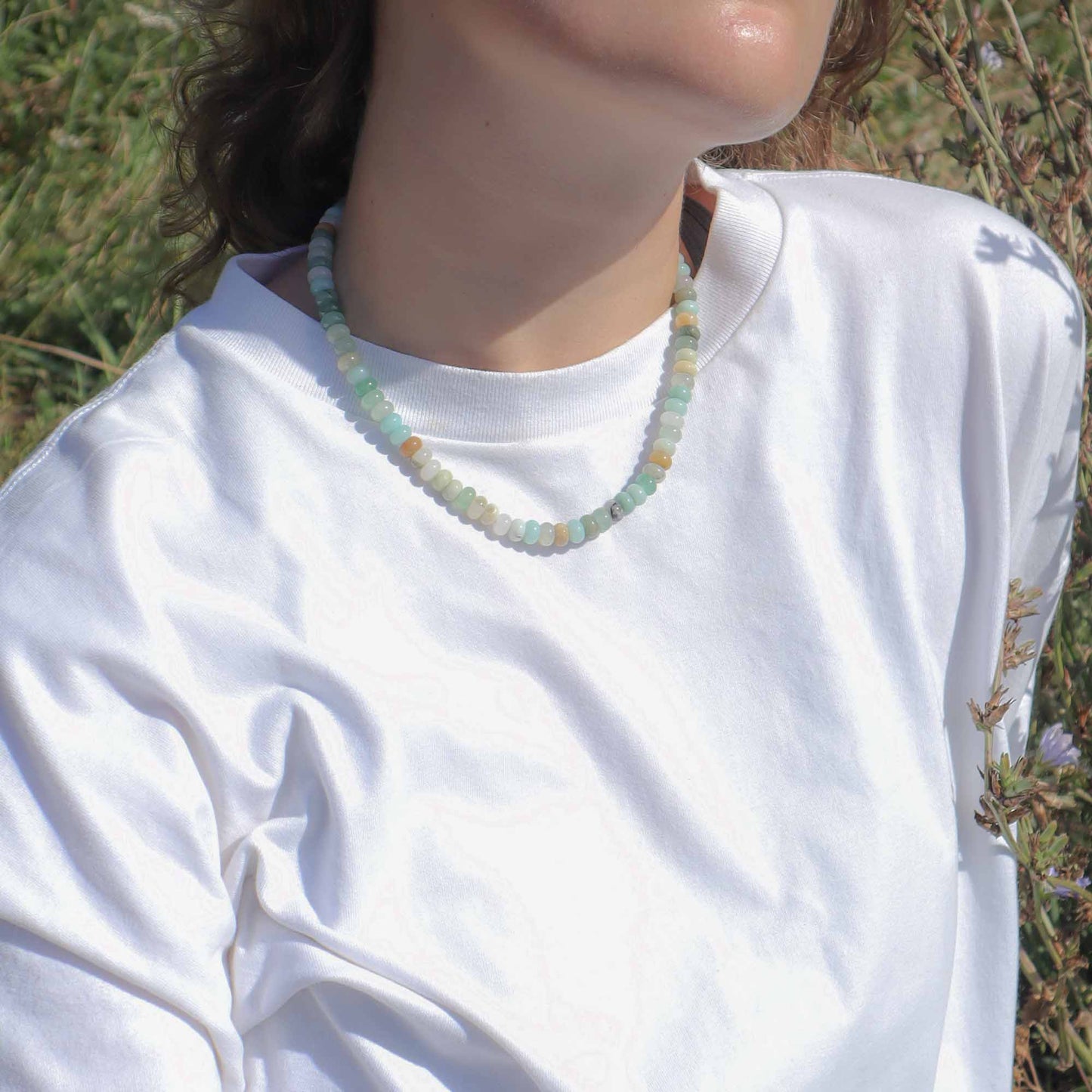 Person wearing a white shirt with a beaded necklace in a natural setting