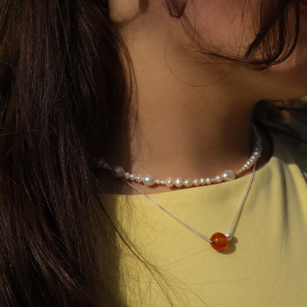 Pearl necklace with a red pendant worn by a person with long dark hair, against a blurred background.