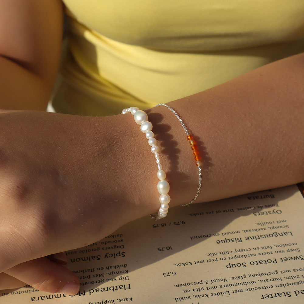 Close-up of a wrist wearing pearl and silver bracelets on a book page.