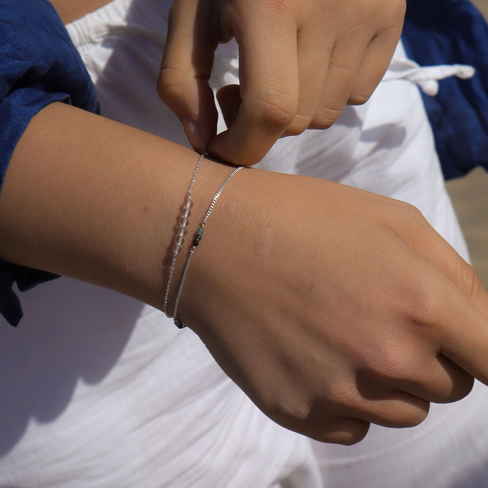 Close-up of a person's wrist with a bracelet, wearing a blue sleeve and white fabric.