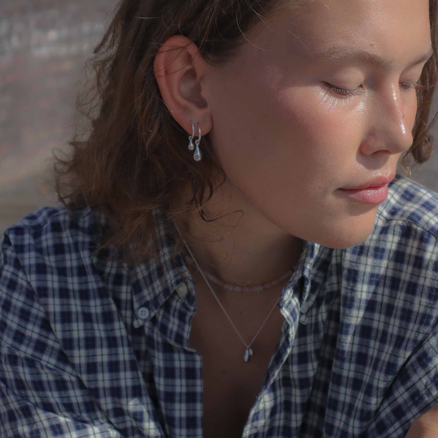 Close-up of a person wearing earrings and a necklace, with a blurred background