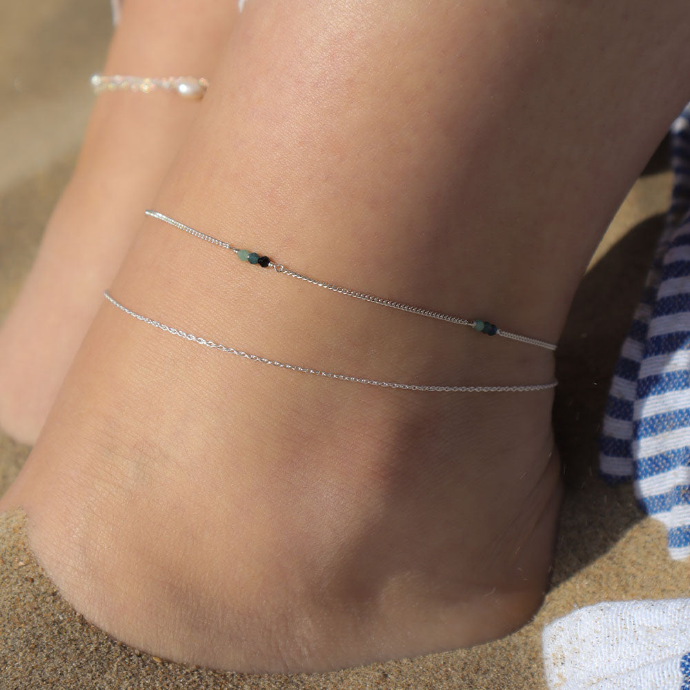 Close-up of a anklet on a person's ankle with sand in the background