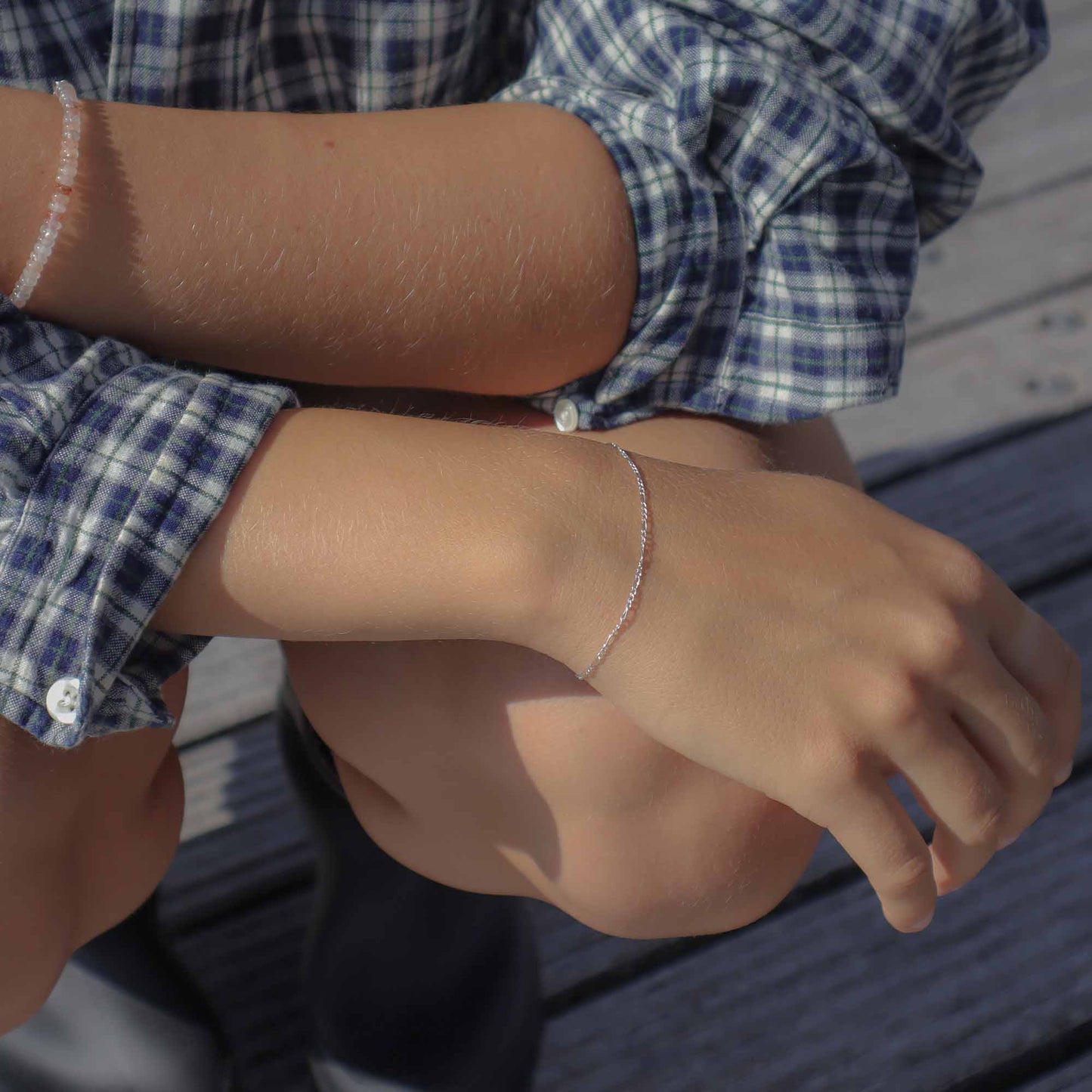 Close-up of a person wearing a blue plaid shirt and bracelet on a wooden surface