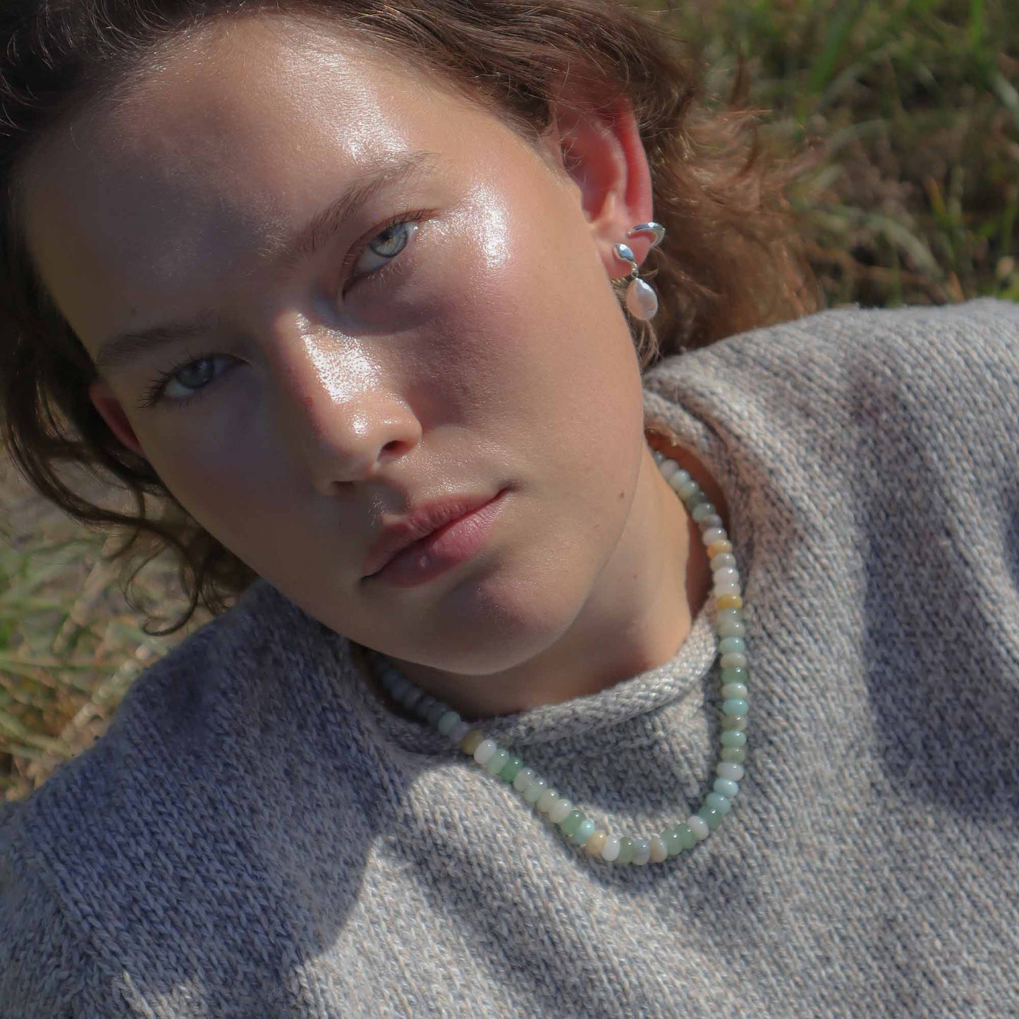 Woman wearing a gray sweater and green beaded necklace outdoors