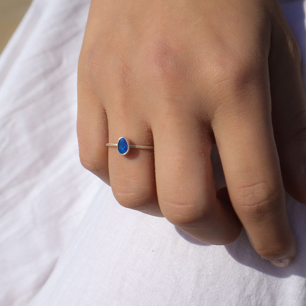 Hand wearing a ring with a blue gemstone on a white fabric background