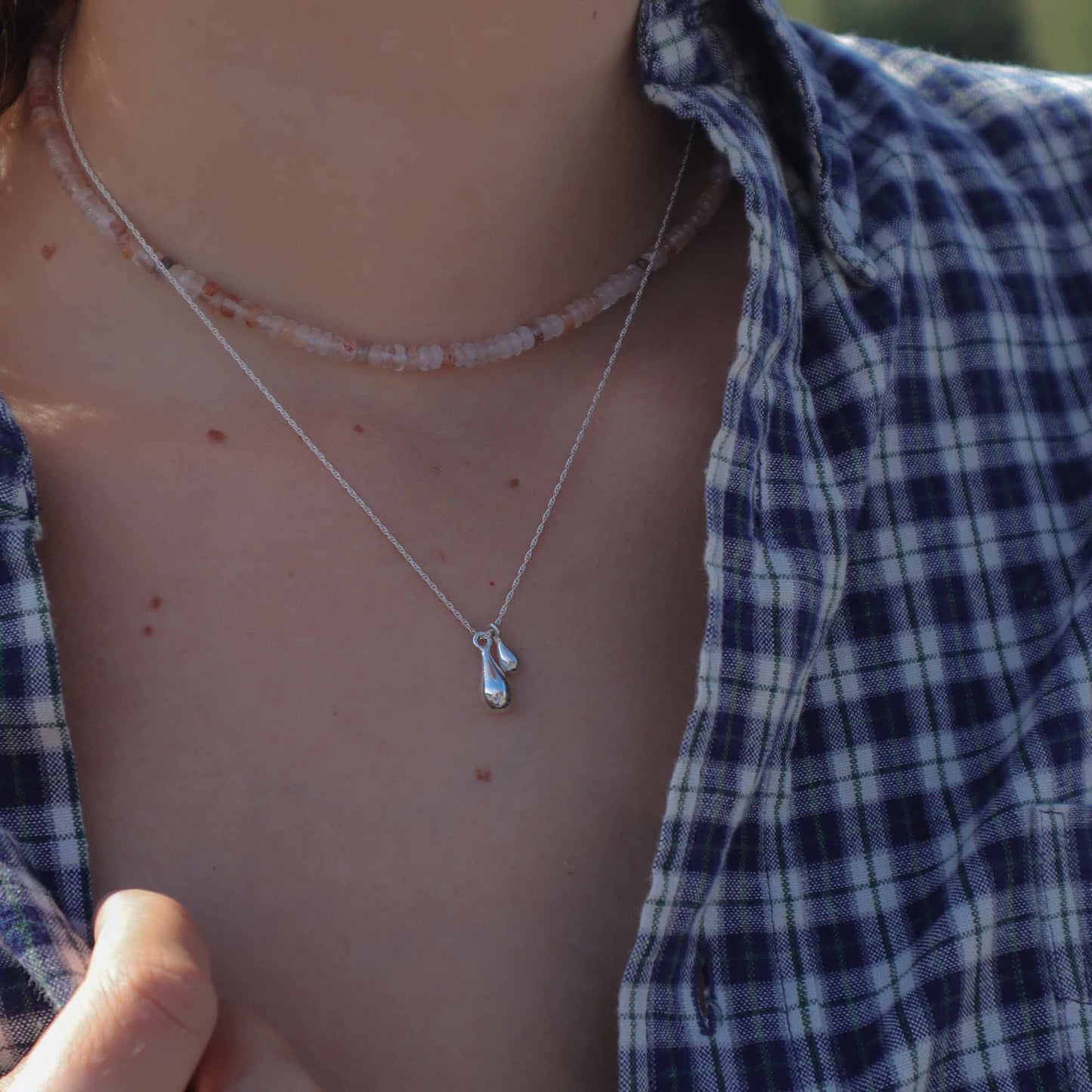 Close-up of a person wearing two necklaces with a blue plaid shirt.