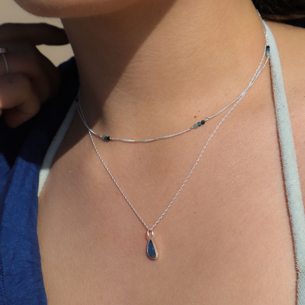 Close-up of a person wearing a silver necklace with a blue pendant.