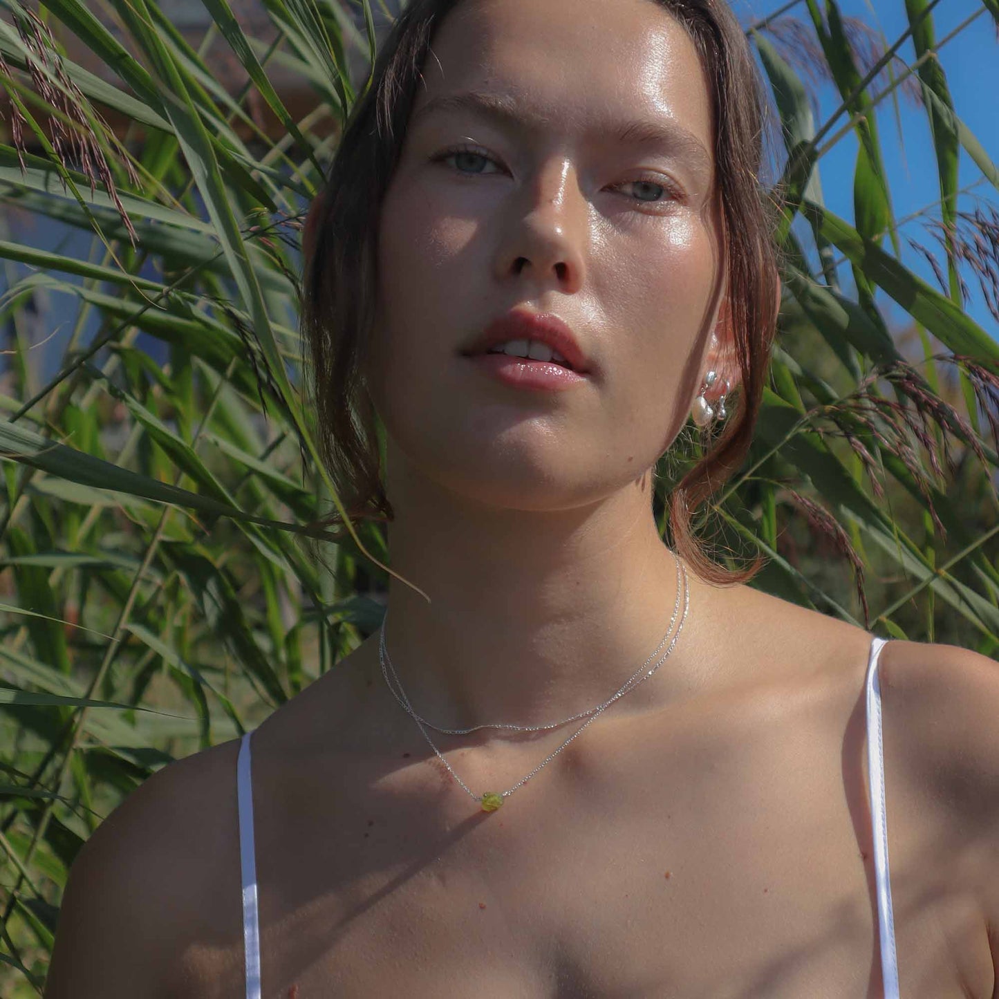 Woman with a white strap top standing in front of green plants