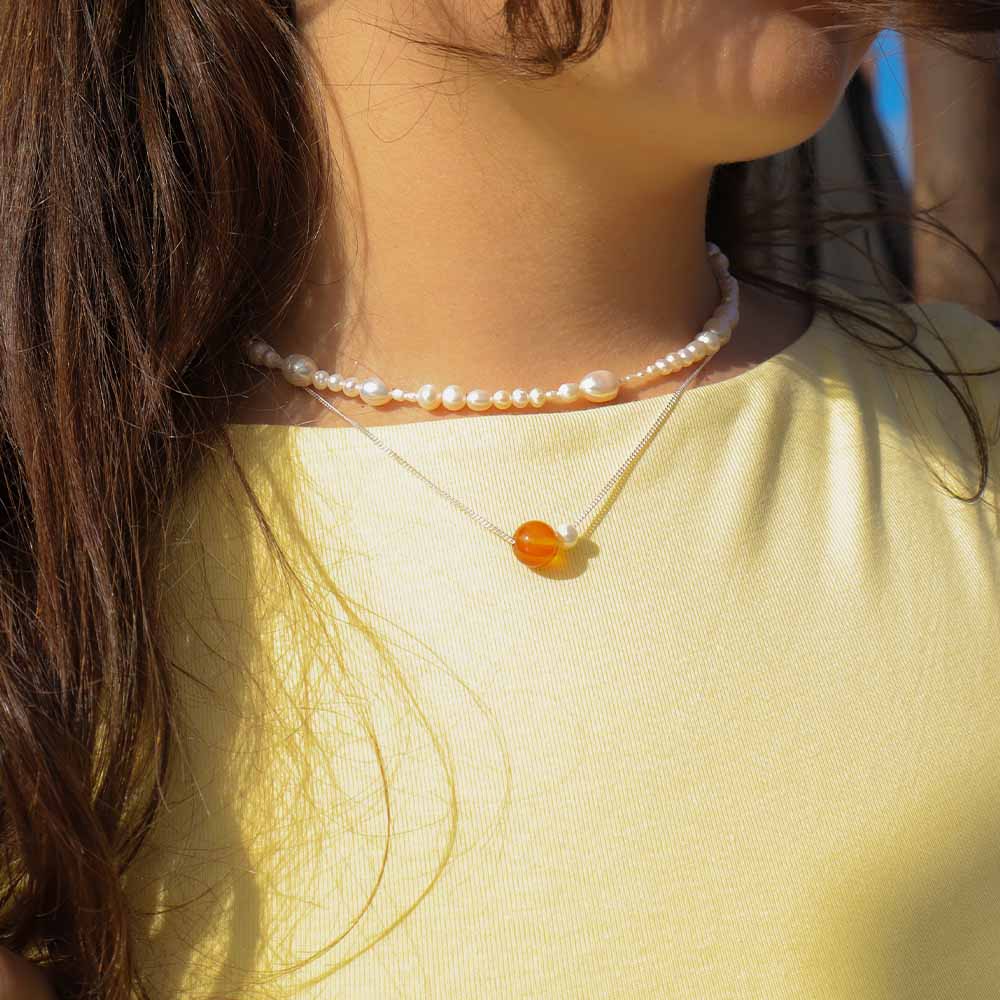 Close-up of a person wearing two necklaces with a yellow shirt.