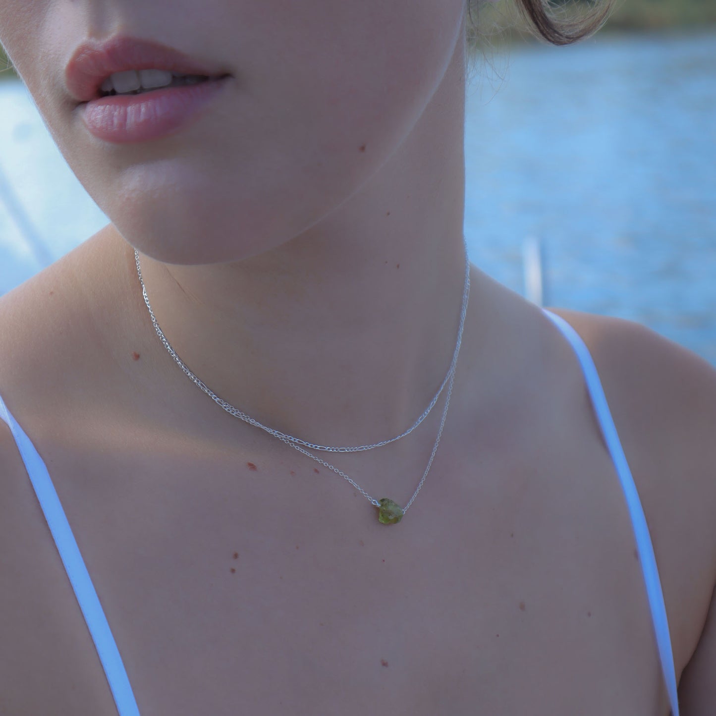 Close-up of a person wearing a silver necklace with a green pendant, outdoors.