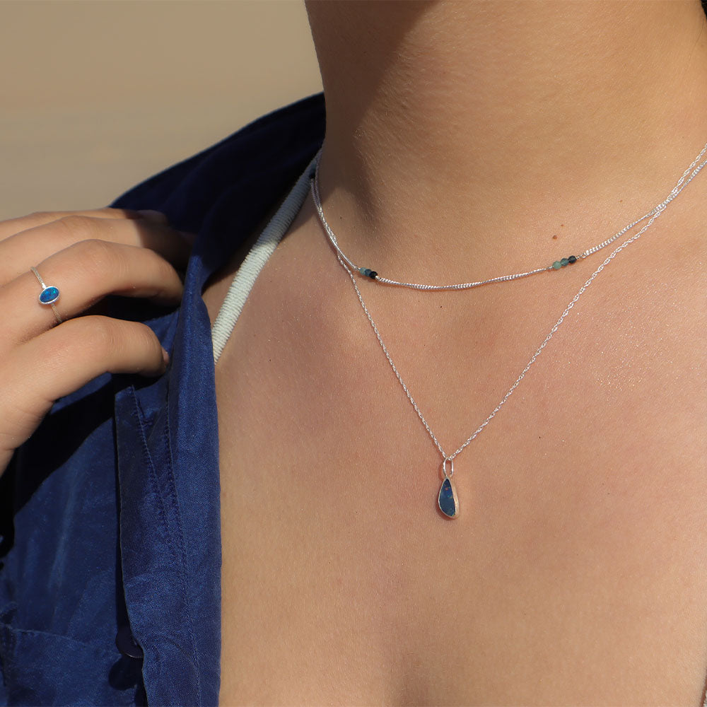 Necklace with a teardrop pendant worn by a person, with a hand adjusting a blue garment.