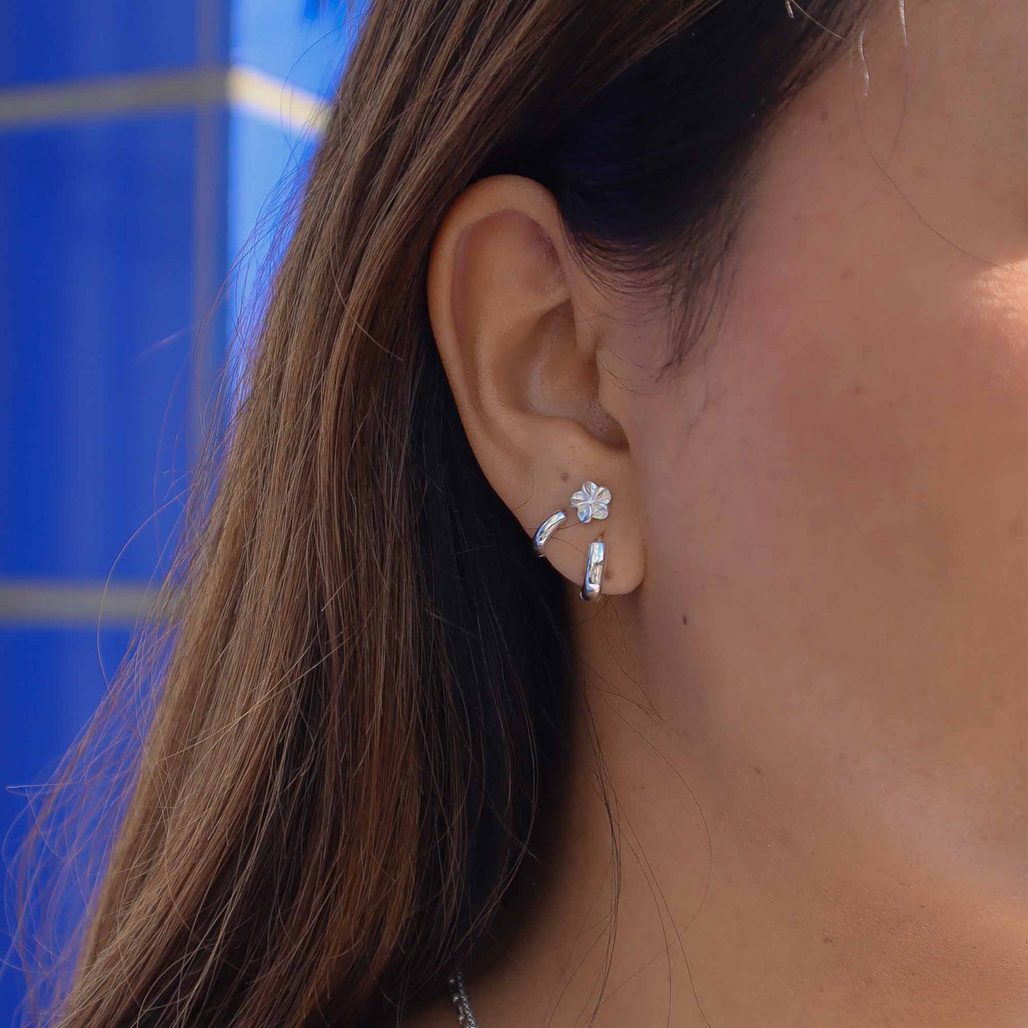 Close-up of an ear wearing a silver earring with a blue background