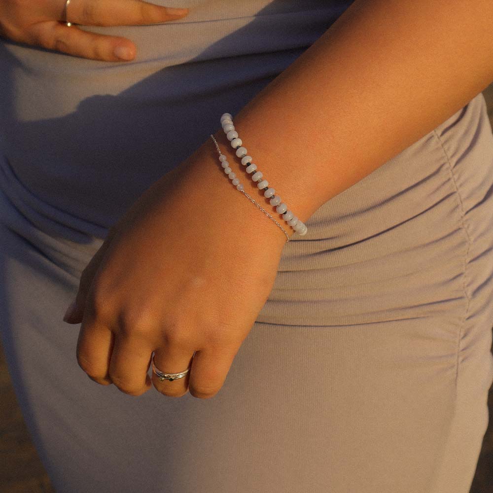 Close-up of a person's wrist with a bracelet and ring, wearing a light-colored garment.