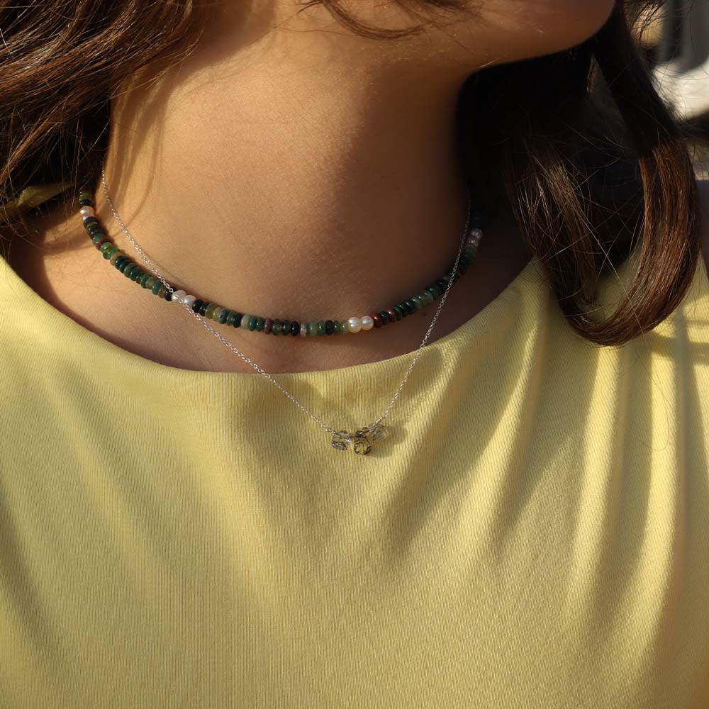 Close-up of a person wearing two necklaces with a yellow shirt.